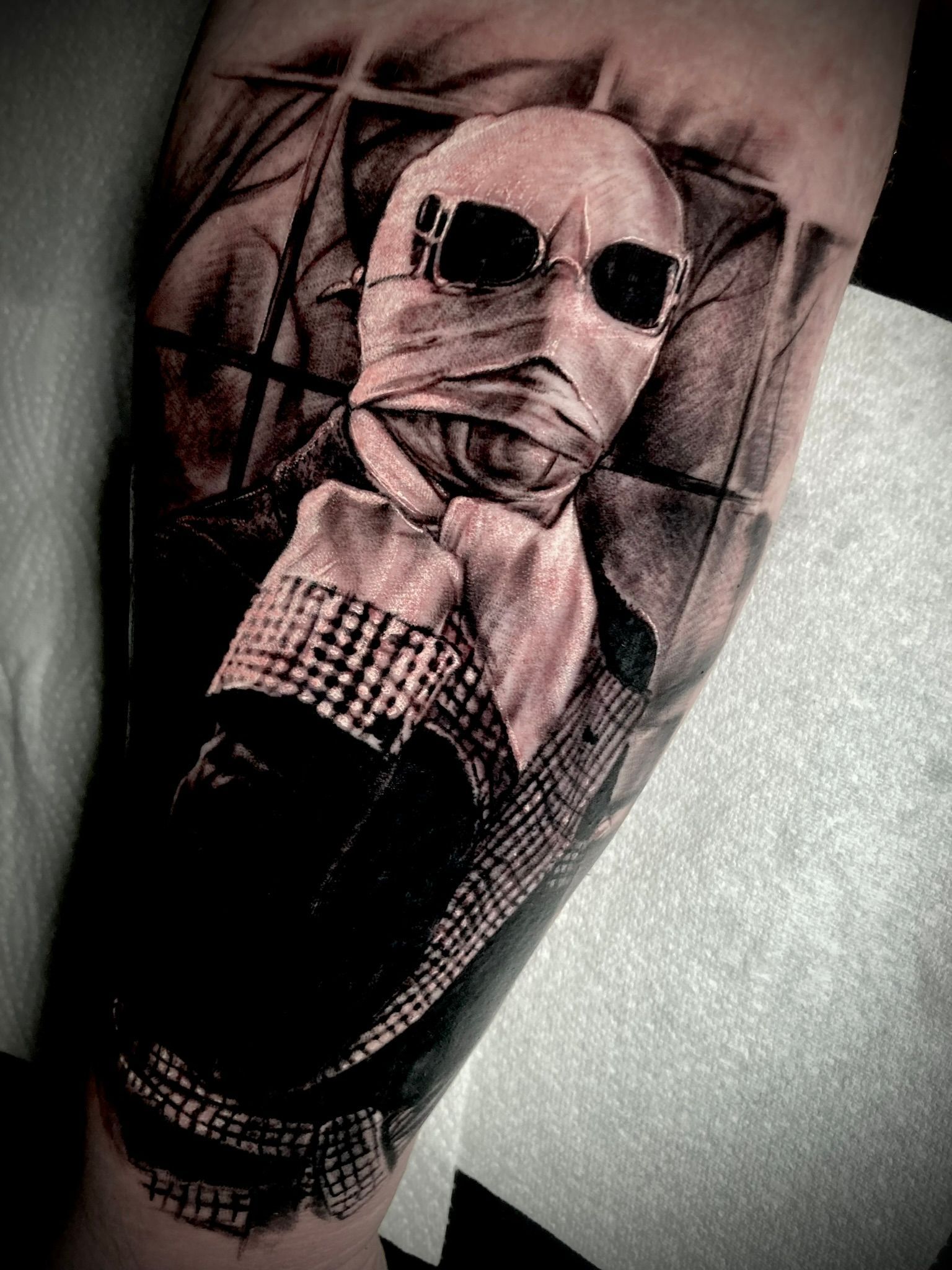 Tattoo of The Invisible Man: wrapped face, dark sunglasses, suit, and checkered cuff.