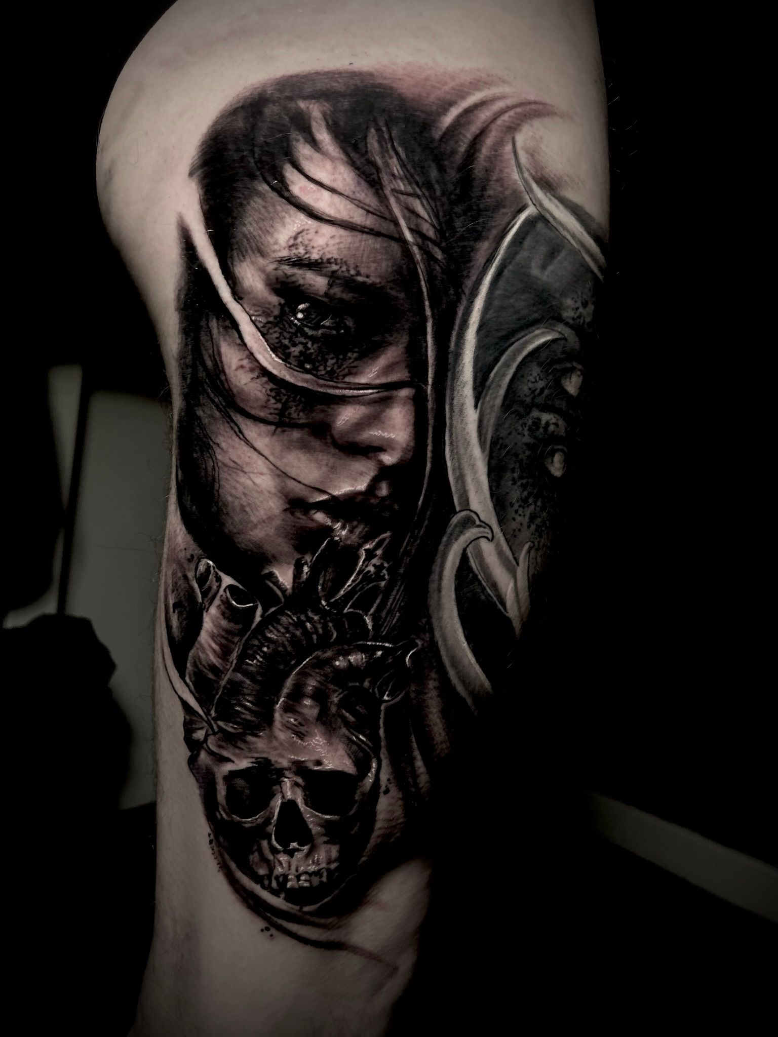 Detailed black and white tattoo on a leg. Features a woman's face, a skull, and decorative elements.