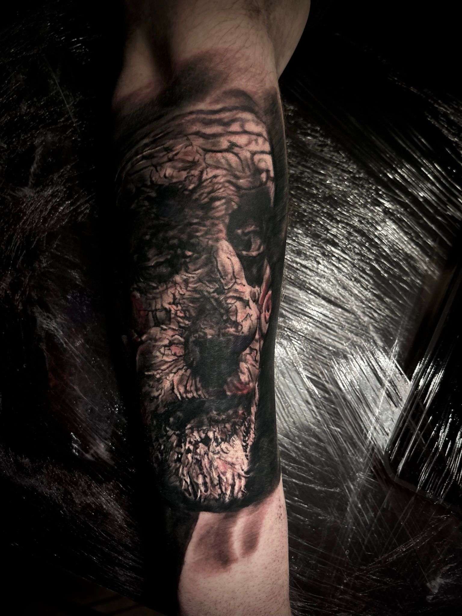 Tattoo of a distorted face in black ink on an arm, with a brick-like texture.