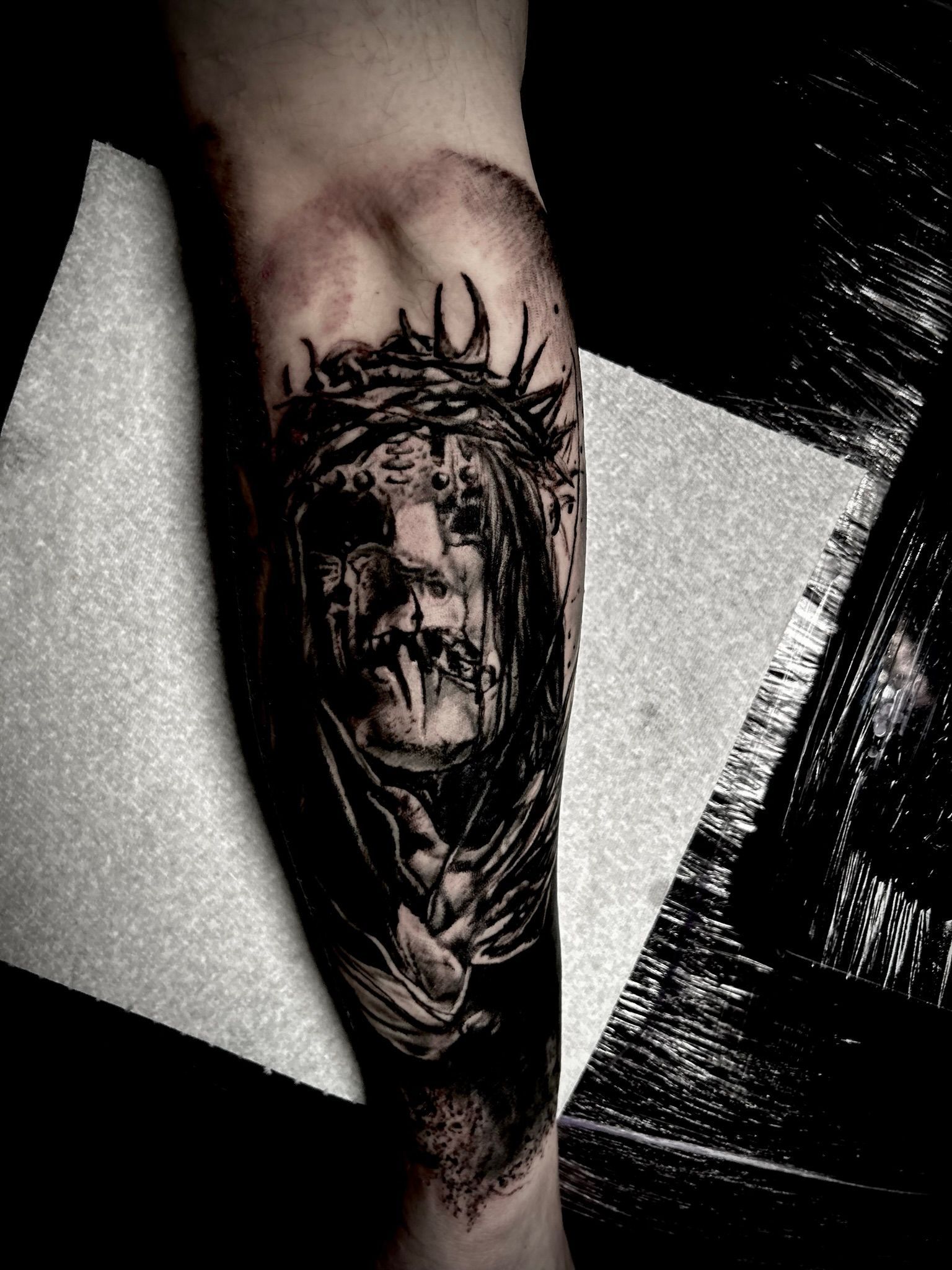 Tattoo of a figure with a crown of thorns, dark, detailed, on an arm.
