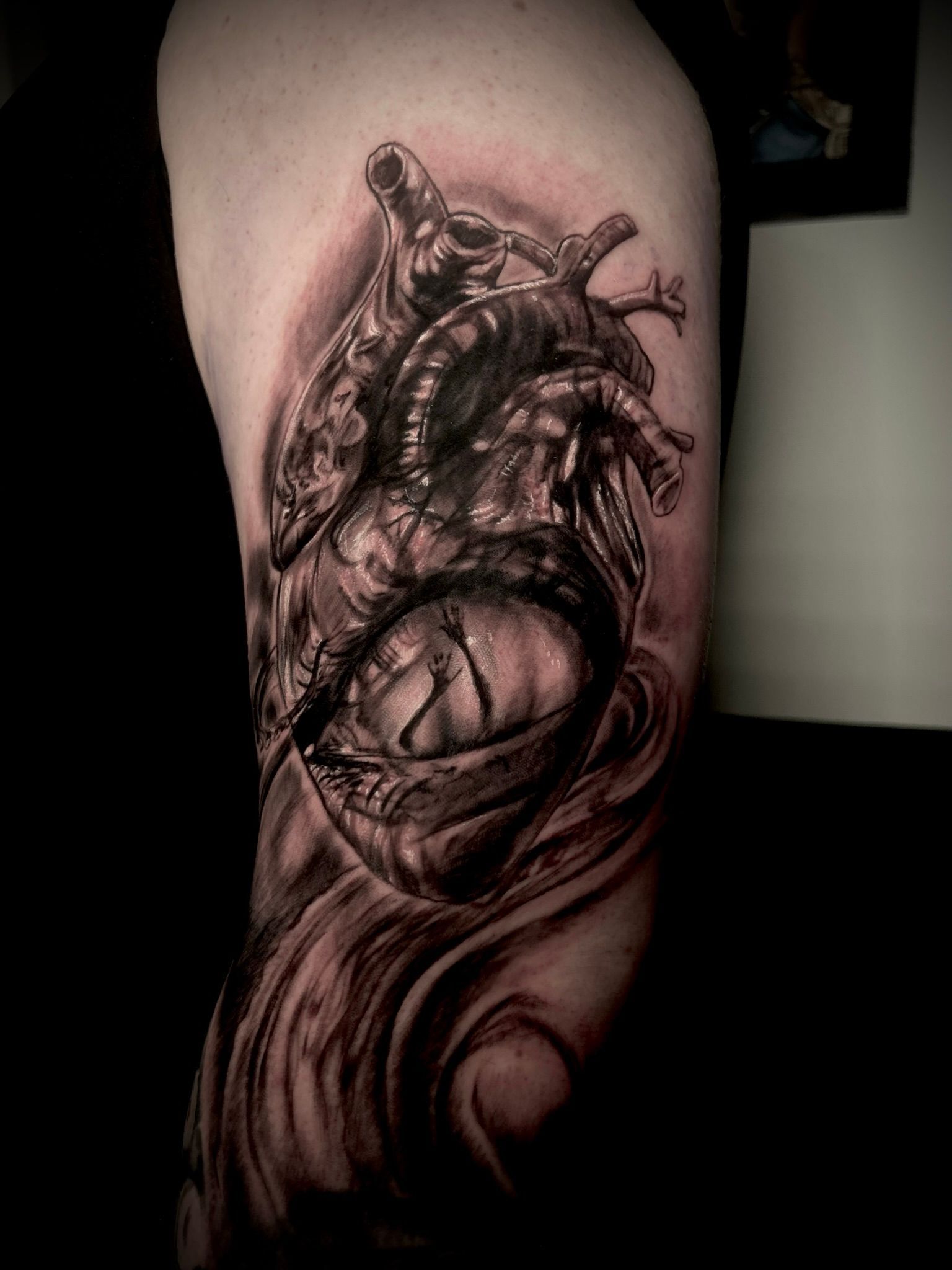 Realistic black and gray anatomical heart tattoo on skin, detailed with shading and swirling design.