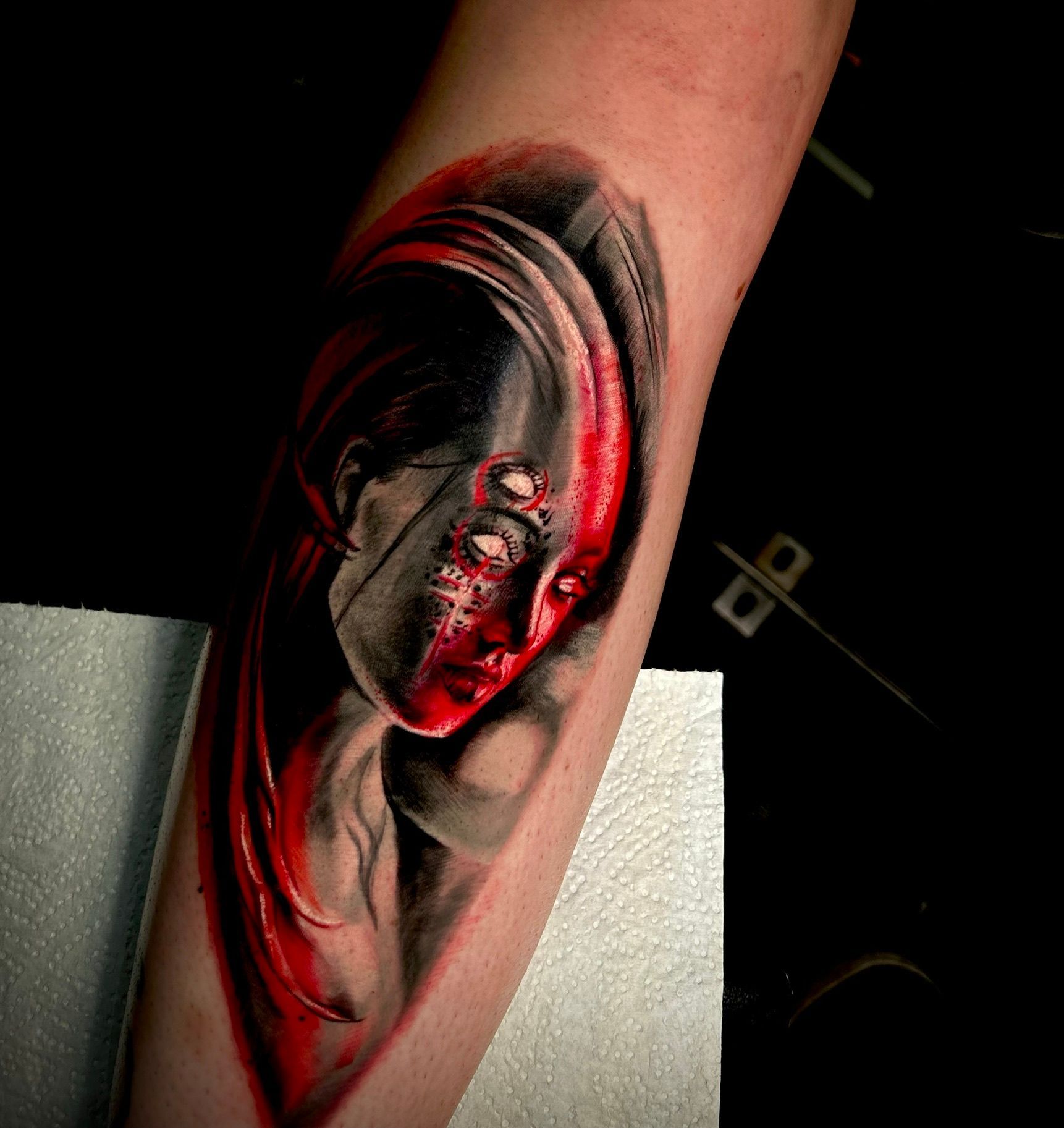 Tattoo of a person's face split with gray and red. The gray side is shadowed, while the red side has multiple eyes.