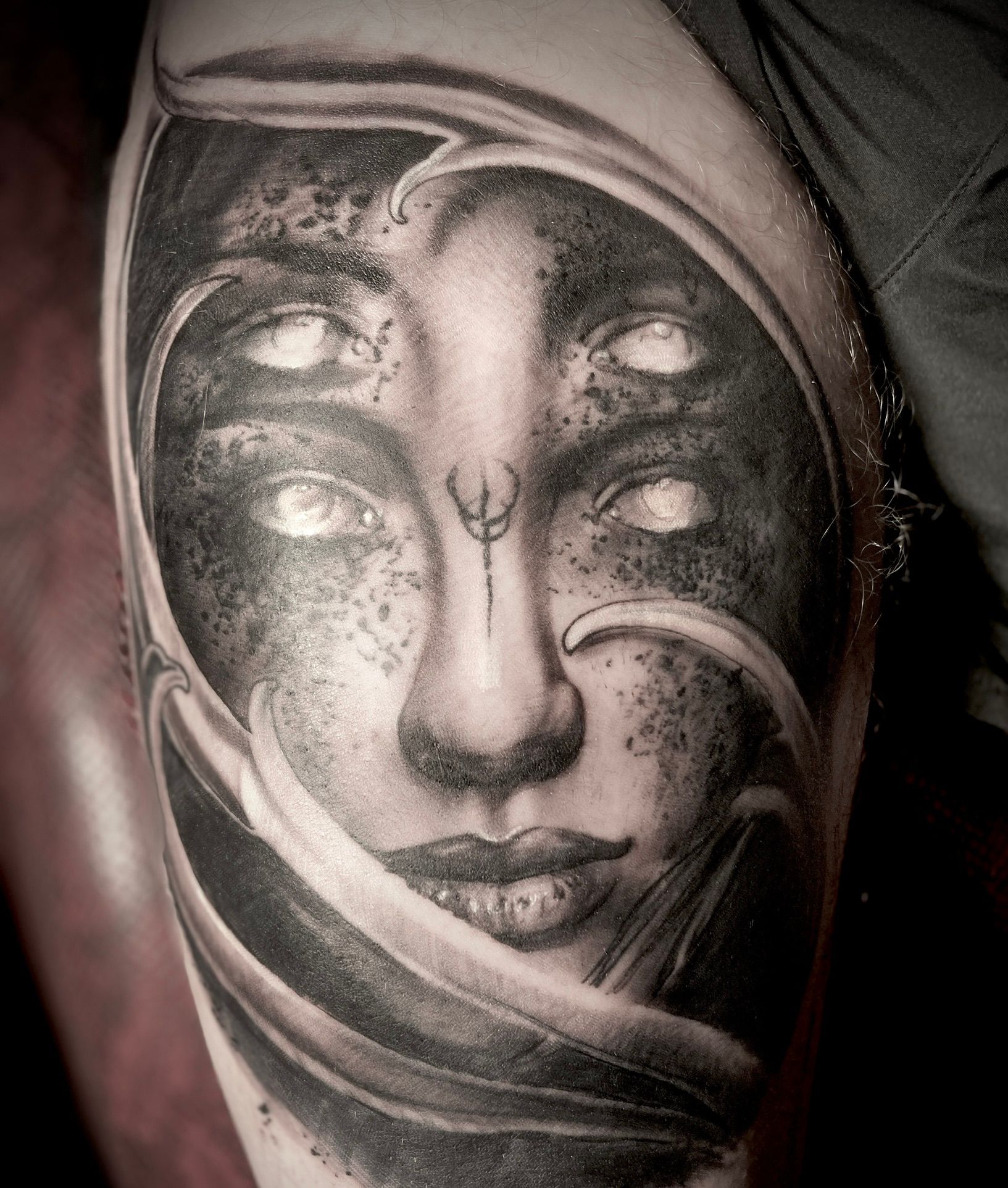 Tattoo of a woman's face with four eyes and flowing lines, shaded in grayscale on the arm.