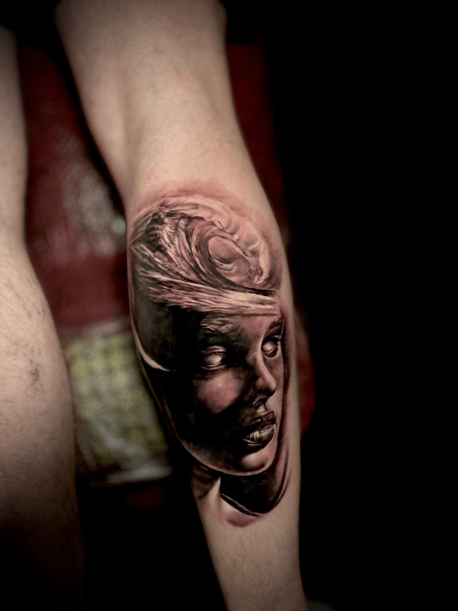 Tattoo of a person's face with waves flowing out from the top of the head in grayscale on a leg.