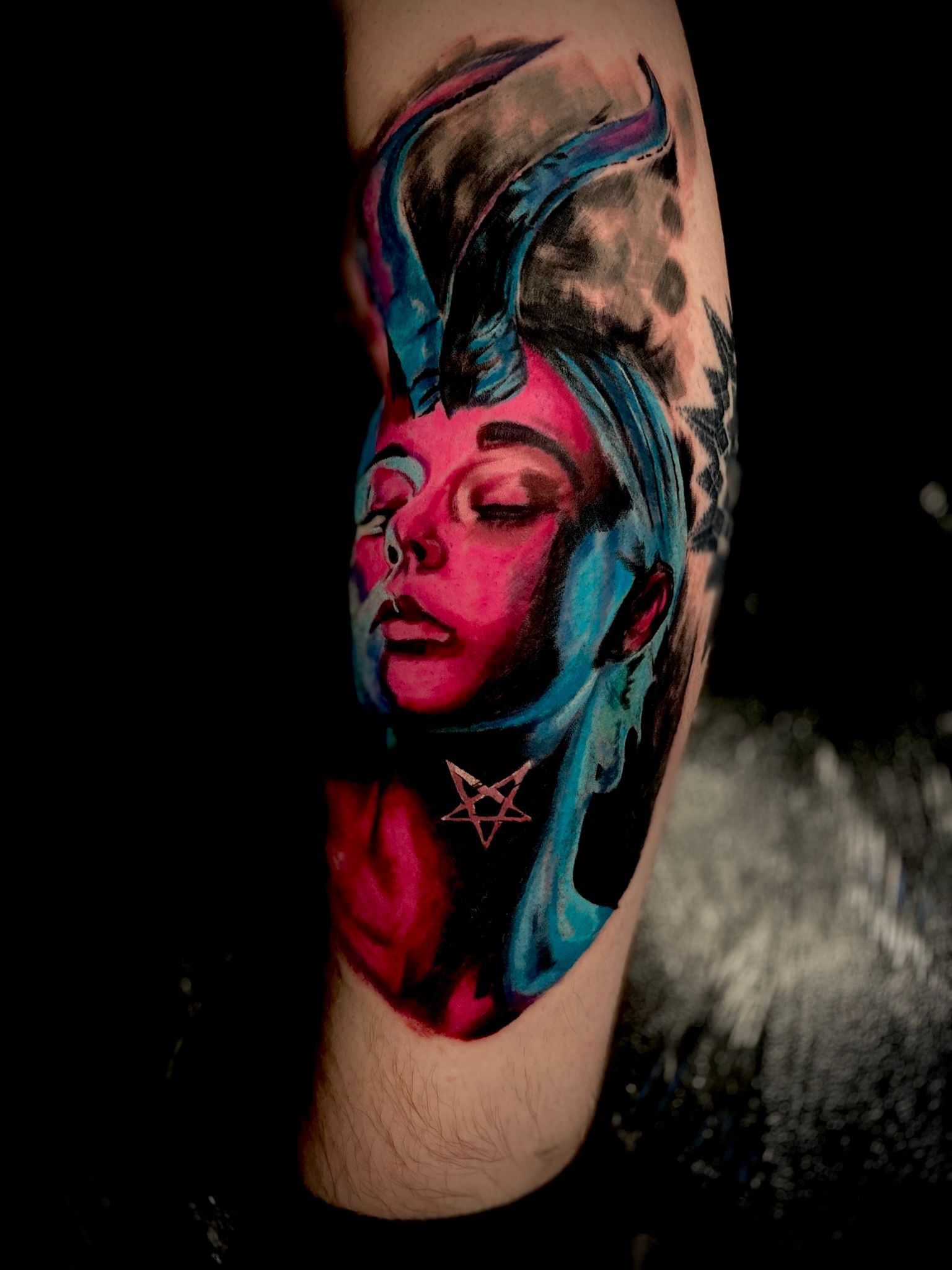 Tattoo of a woman with blue horns and face partially painted blue and pink; a pentagram necklace is visible.