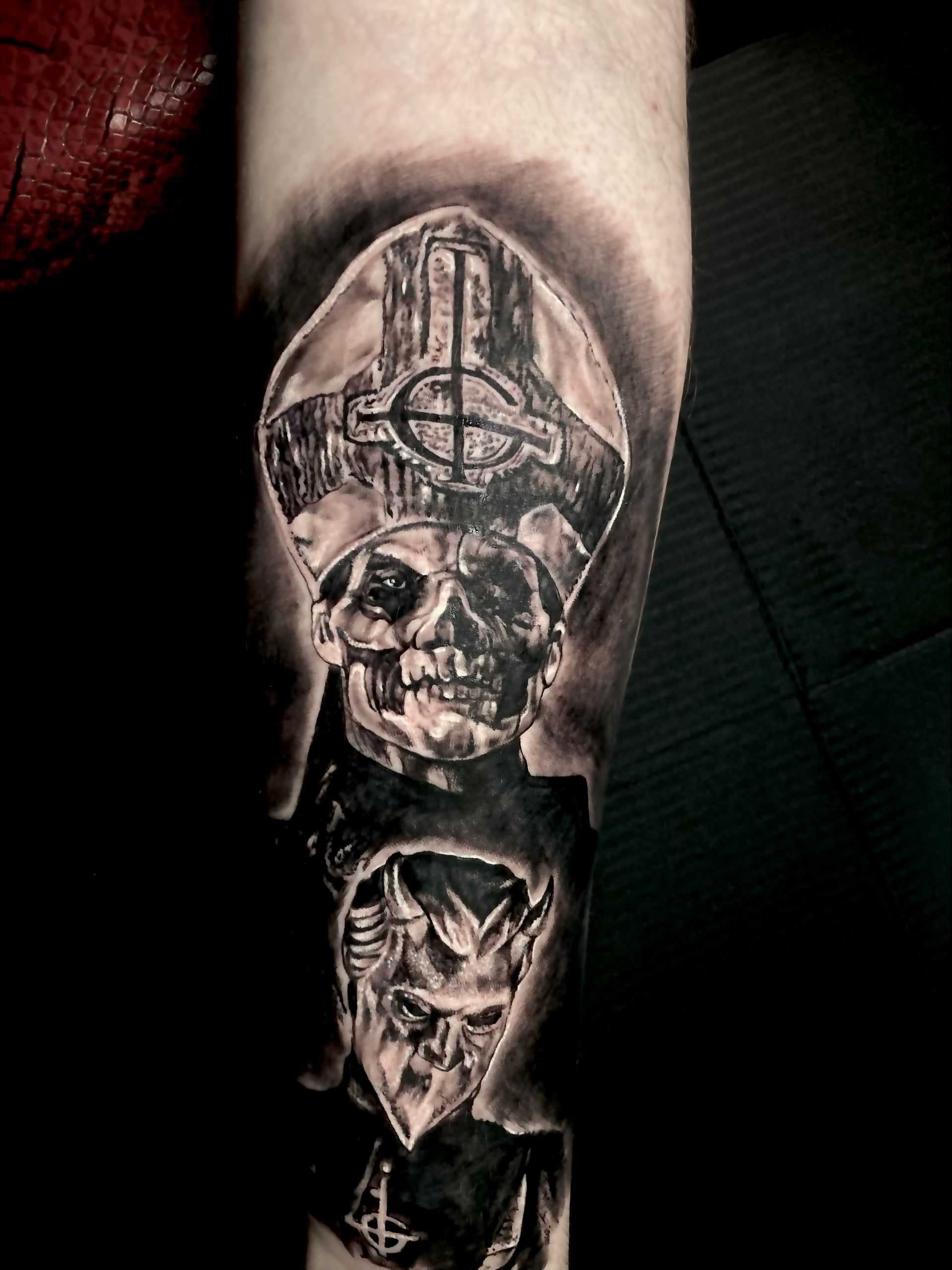 Tattoo of a skull-faced figure wearing a bishop's hat, black and white, on an arm.