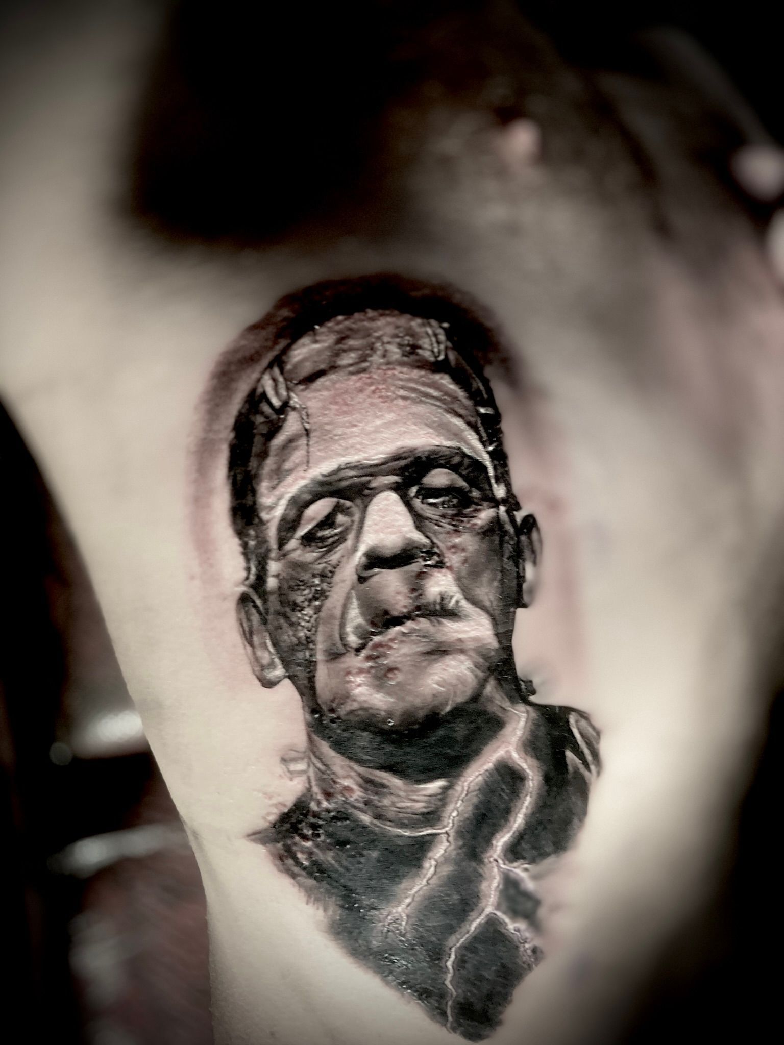 Black and white tattoo of Frankenstein's monster on a person's torso, featuring scars and a pensive expression.