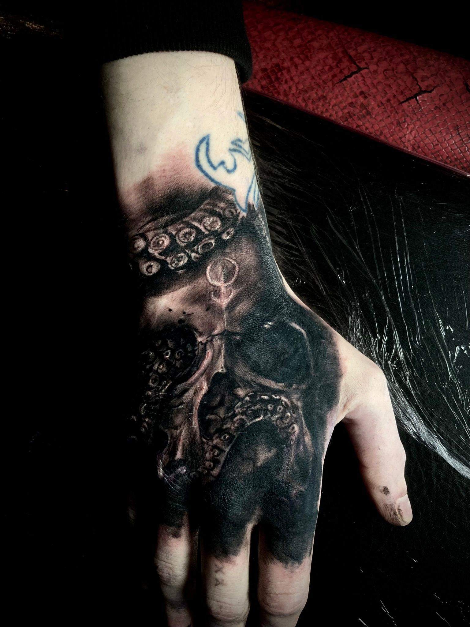Hand tattoo: dark skull with tentacles, partial black ink cover, visible skin.