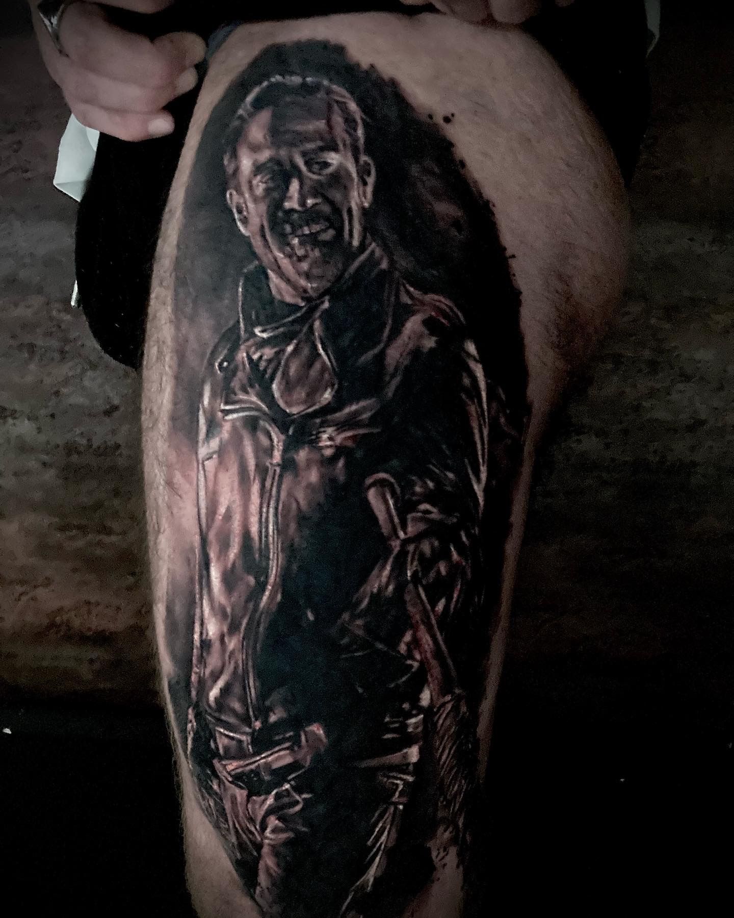Tattoo of a person in a leather jacket, holding a weapon. Black and gray shading with visible face on leg.