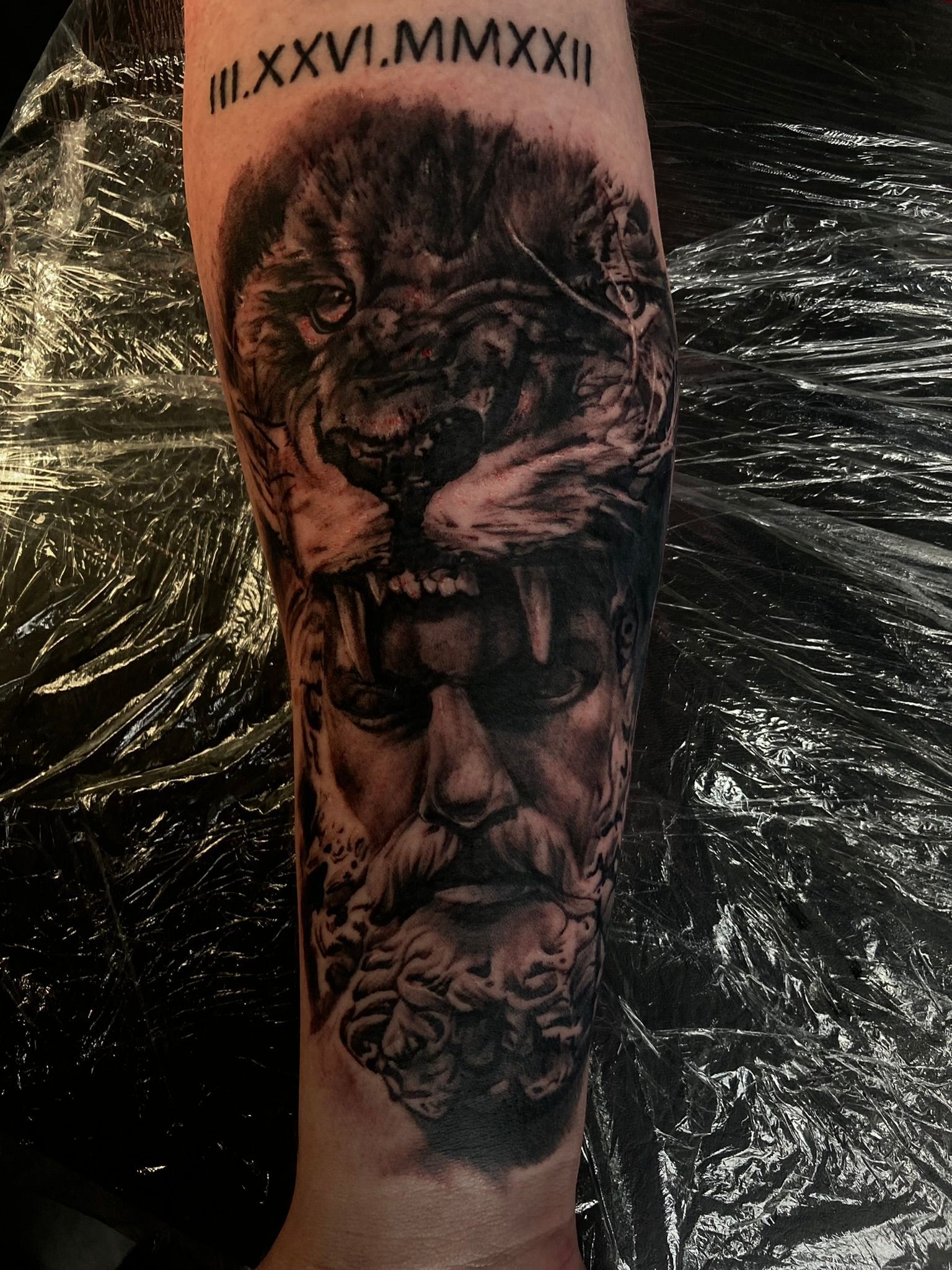 Tattoo of a lion's head over the face of a man with a beard and roman numerals at the top.