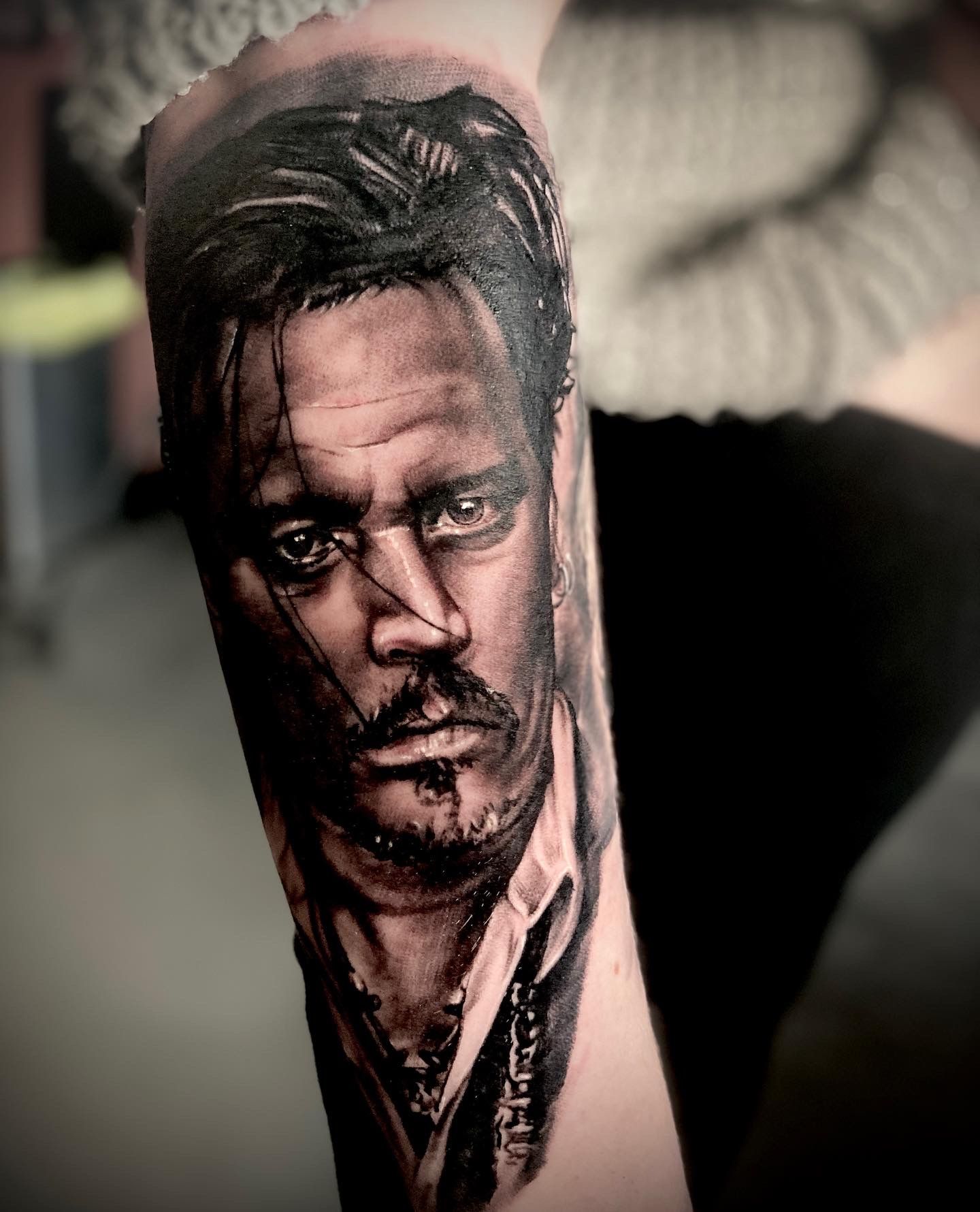 Tattoo of Johnny Depp as Captain Jack Sparrow on a person's forearm, black and gray portrait.