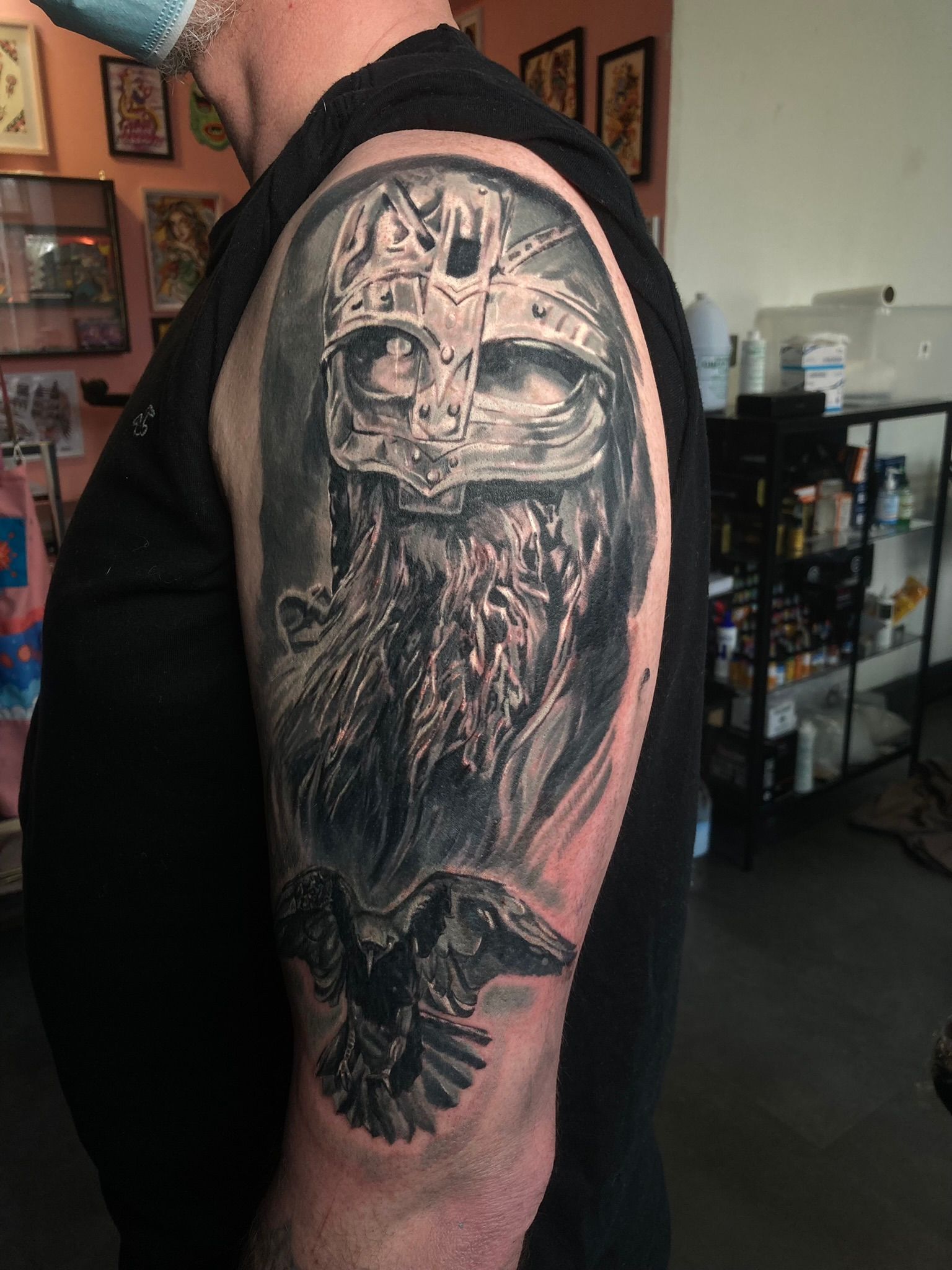 Tattoo of a Viking with a horned helmet and raven on a man's arm, in a tattoo parlor.