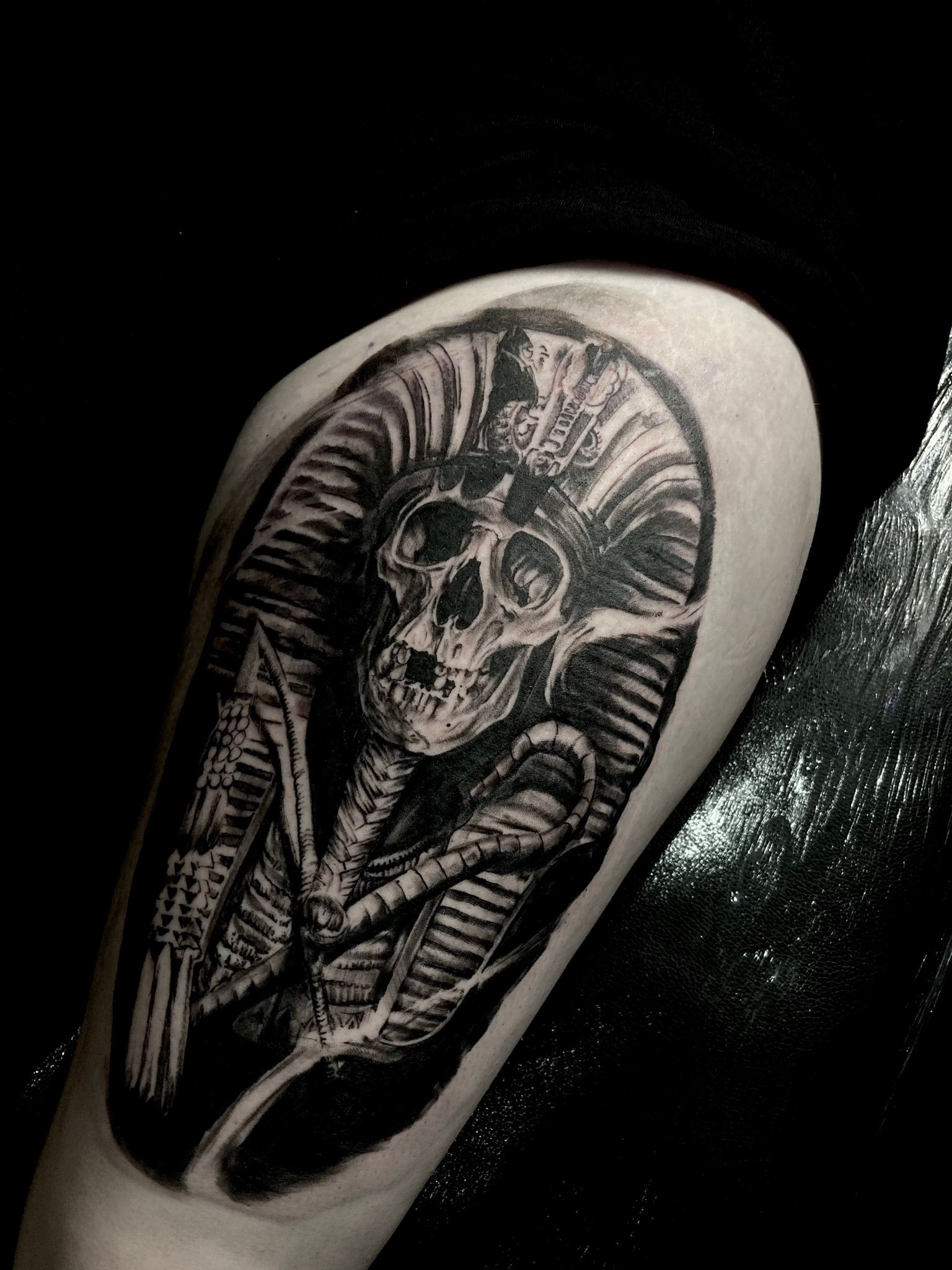 Black tattoo of a skull wearing a crown, wrapped in a cocoon-like design, on a person's arm.