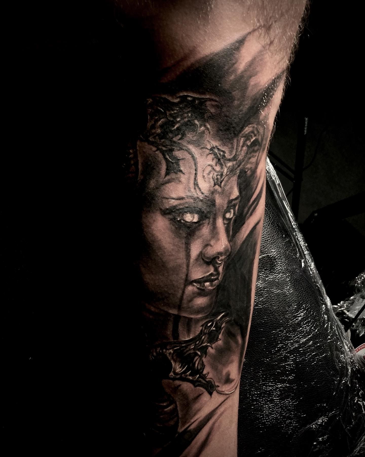 Black and grey tattoo of a woman with glowing eyes and intricate facial details on an arm.