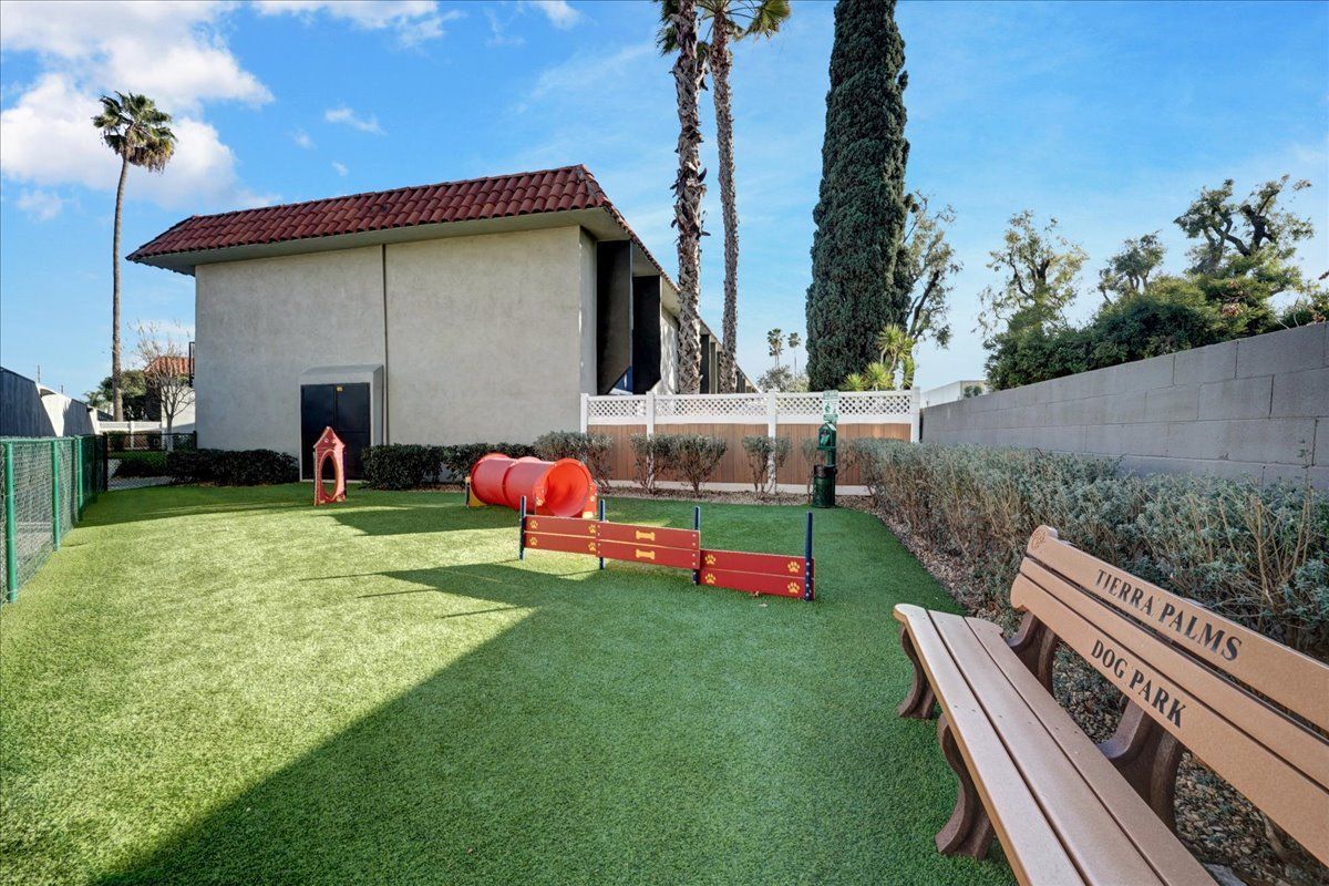 A dog park with a bench in the foreground and a building in the background.