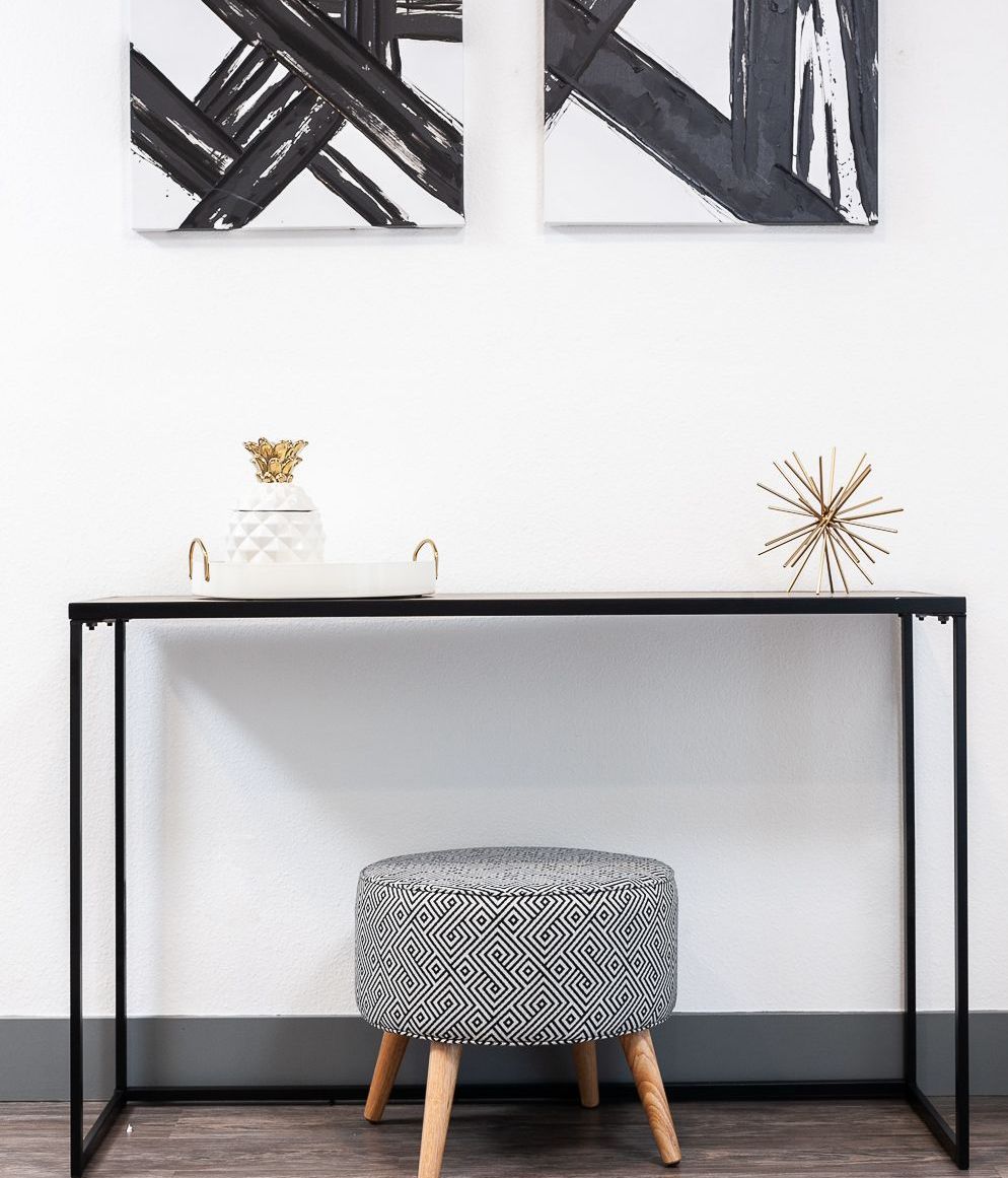 A black and white ottoman is sitting under a table with two paintings on the wall above it.