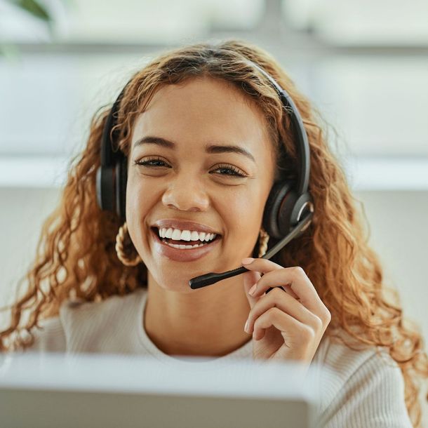 A woman wearing headphones is smiling while sitting in front of a computer.