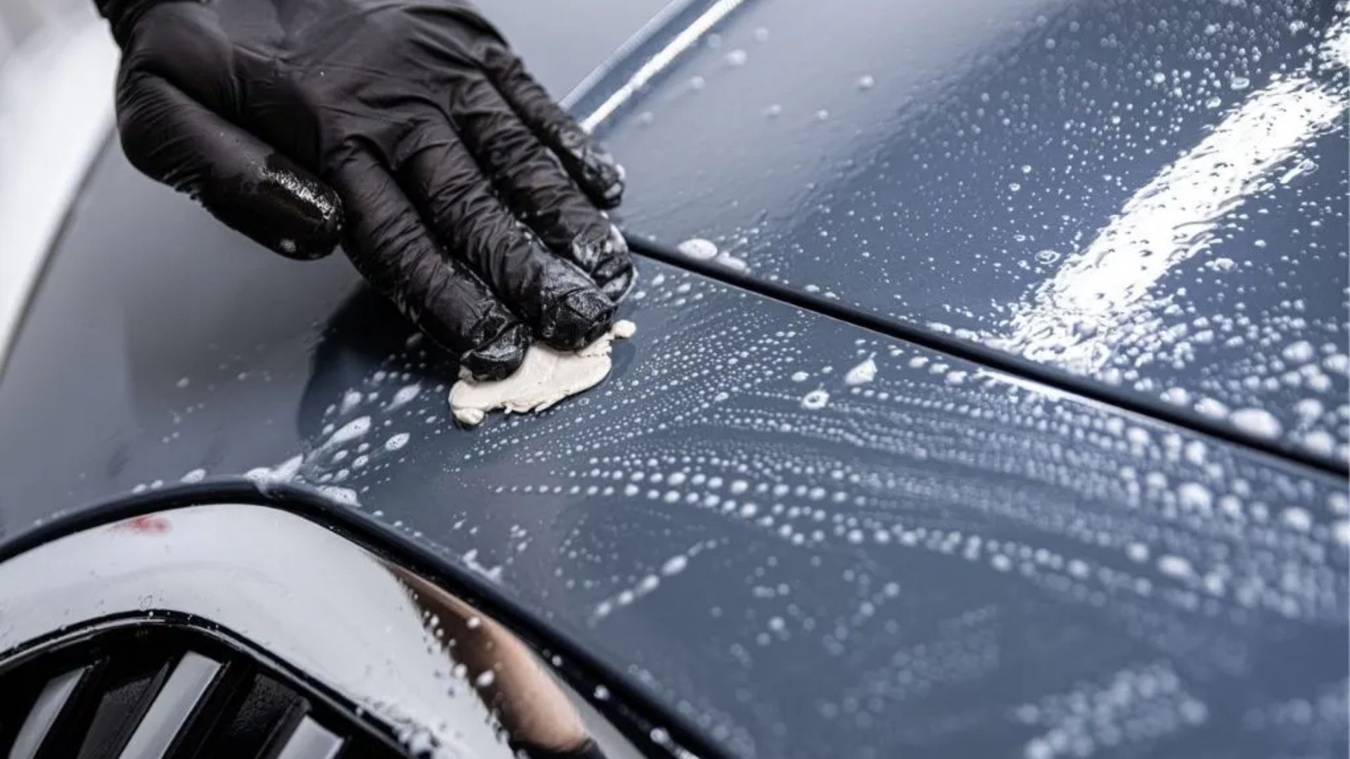 A person wearing black gloves is cleaning a car with a sponge.