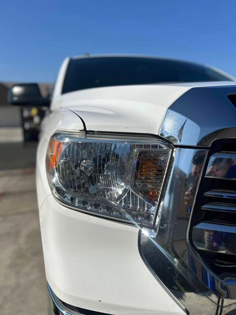A close up of a white truck 's headlight and grille.