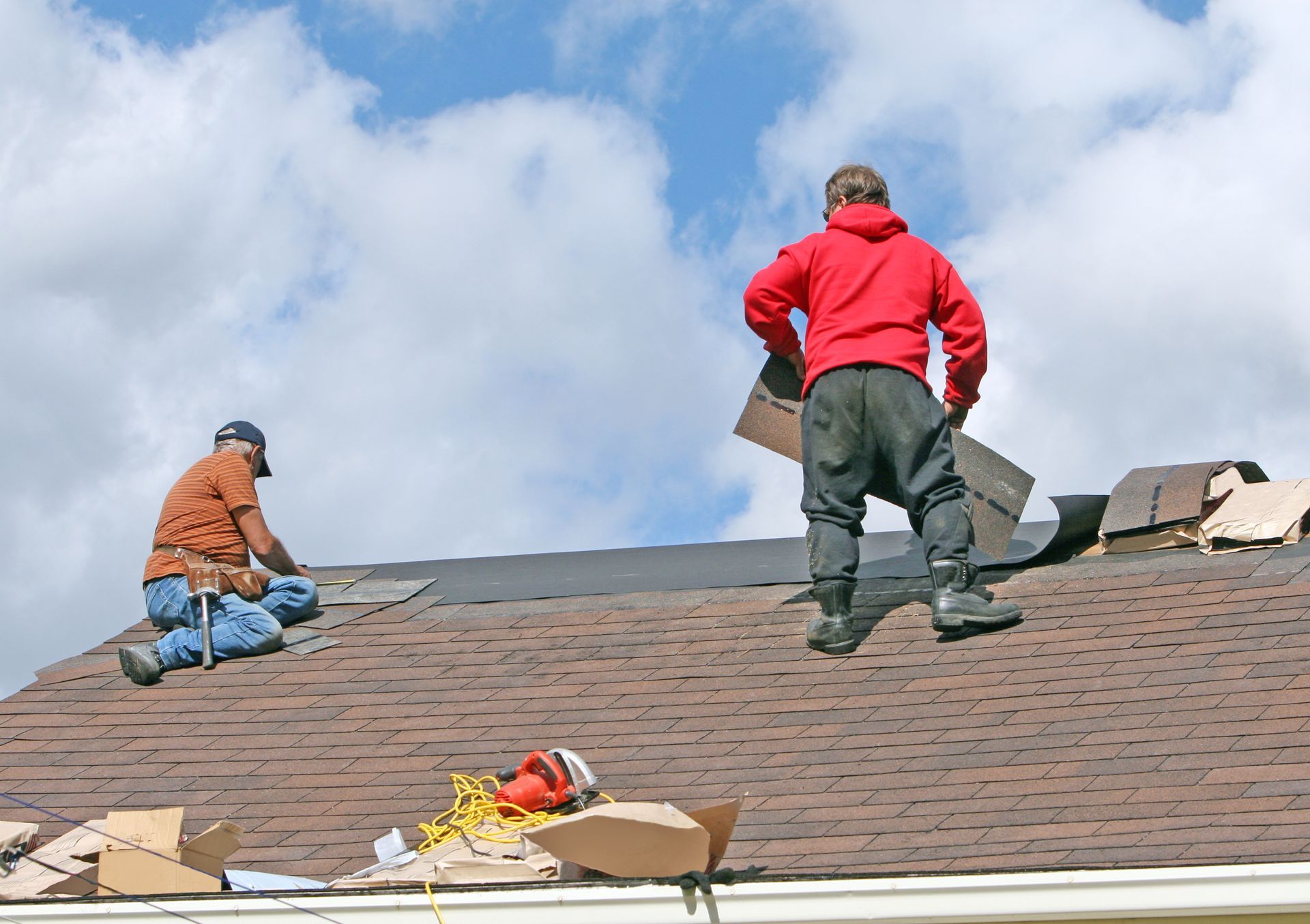 Two professional male contractors completing a roof repair job at a residential site.