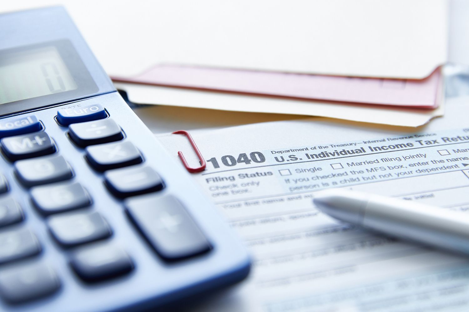 Calculator, tax form, pen, and file folders; preparing taxes.
