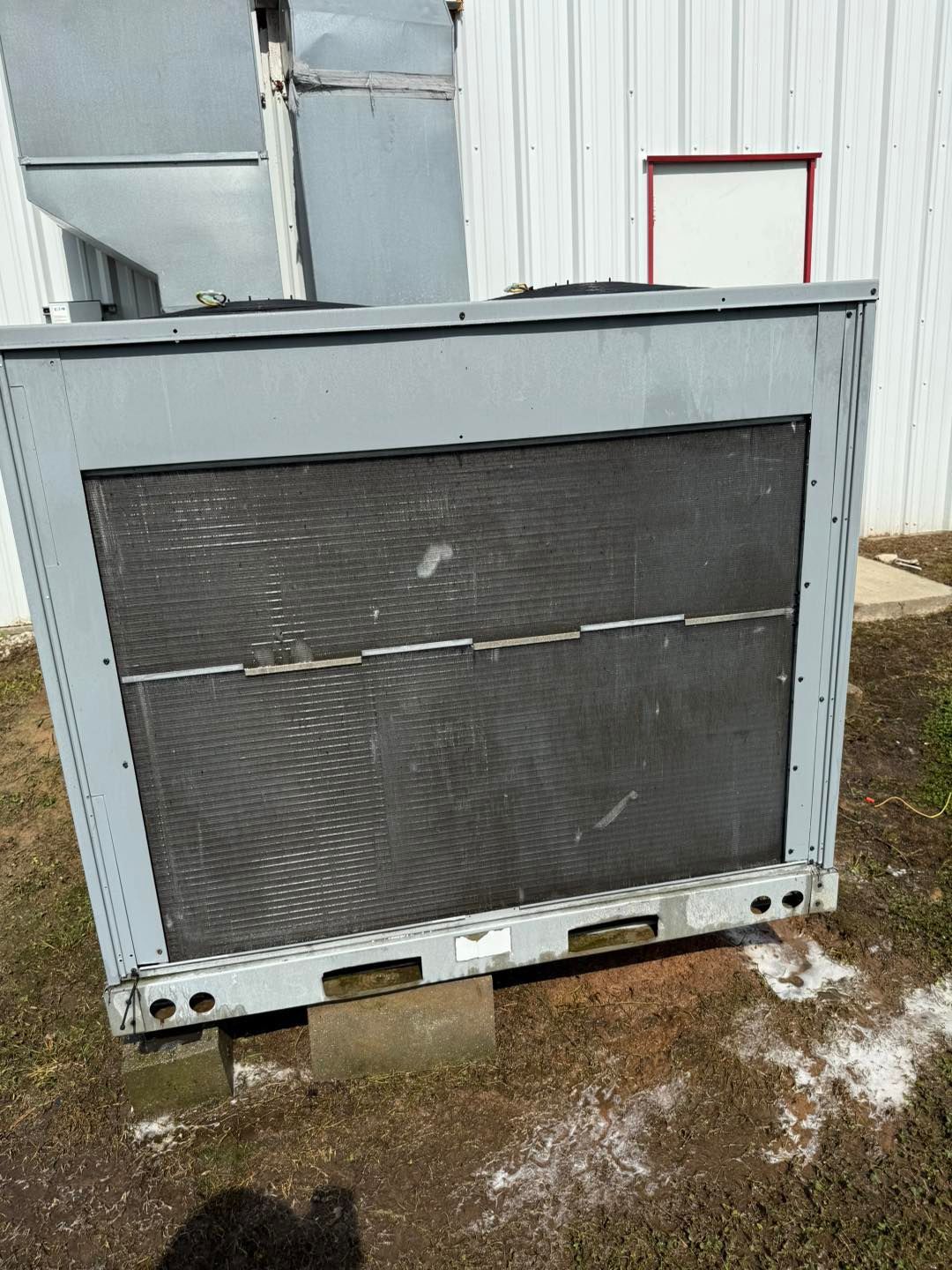 Gray HVAC unit with a large black mesh screen against a white building.