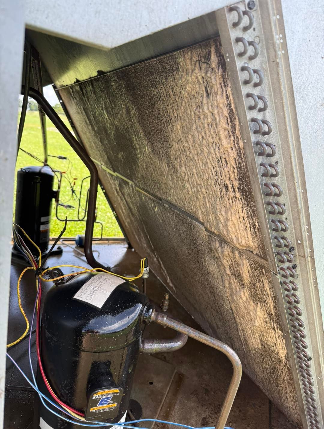 AC unit's condenser coil coated with debris, beside a compressor in an outdoor setting.