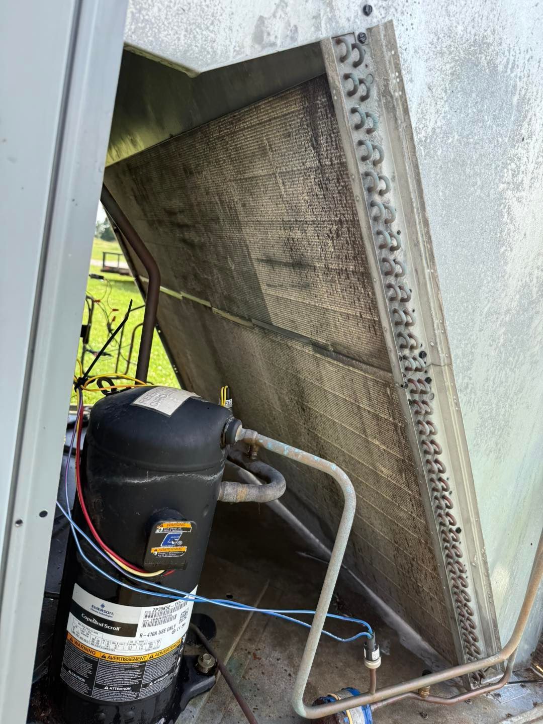 HVAC unit with dirty cooling coils and black compressor.