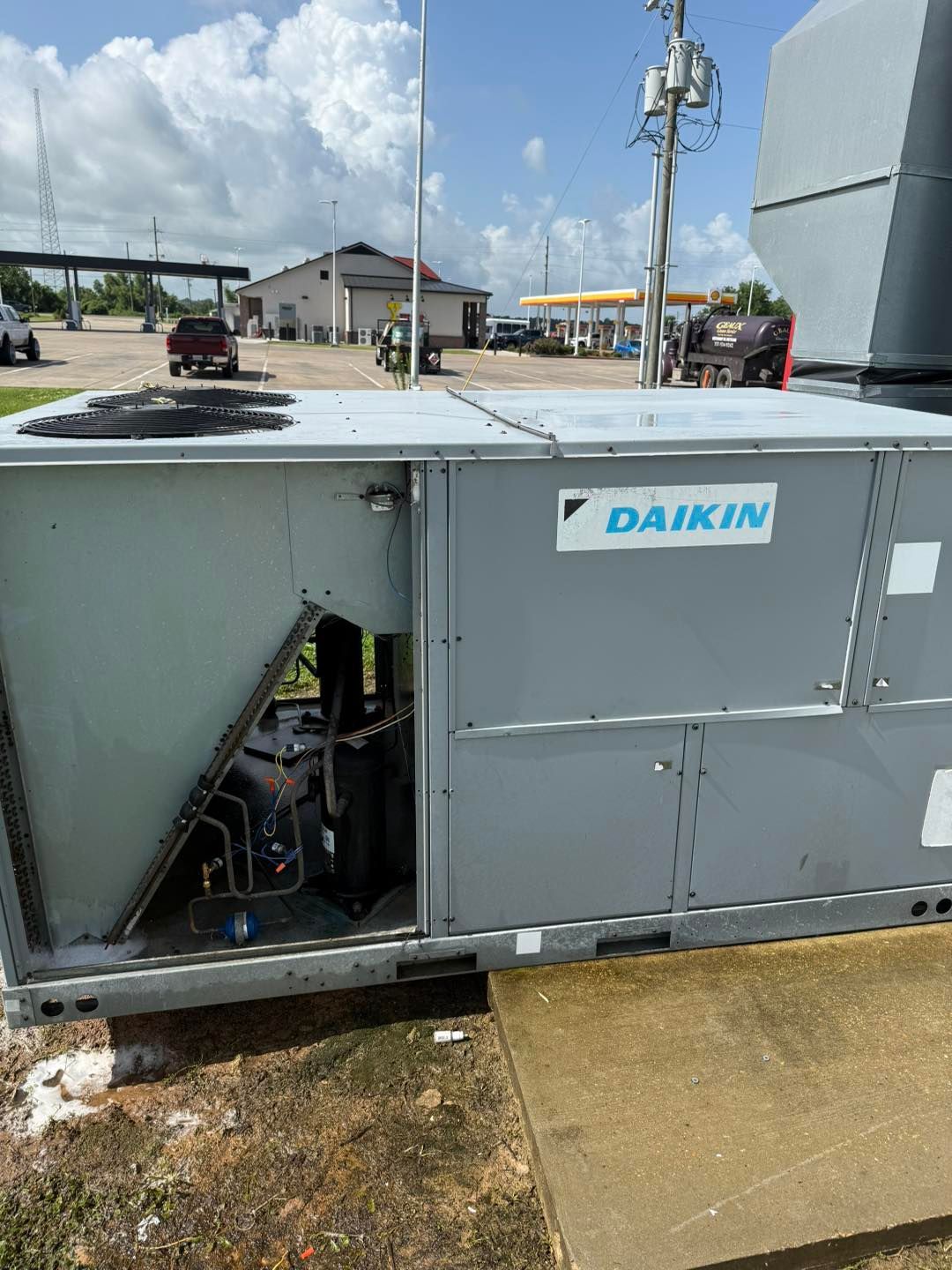 Daikin HVAC unit on a building roof, with open access panel. Nearby gas station and blue sky.
