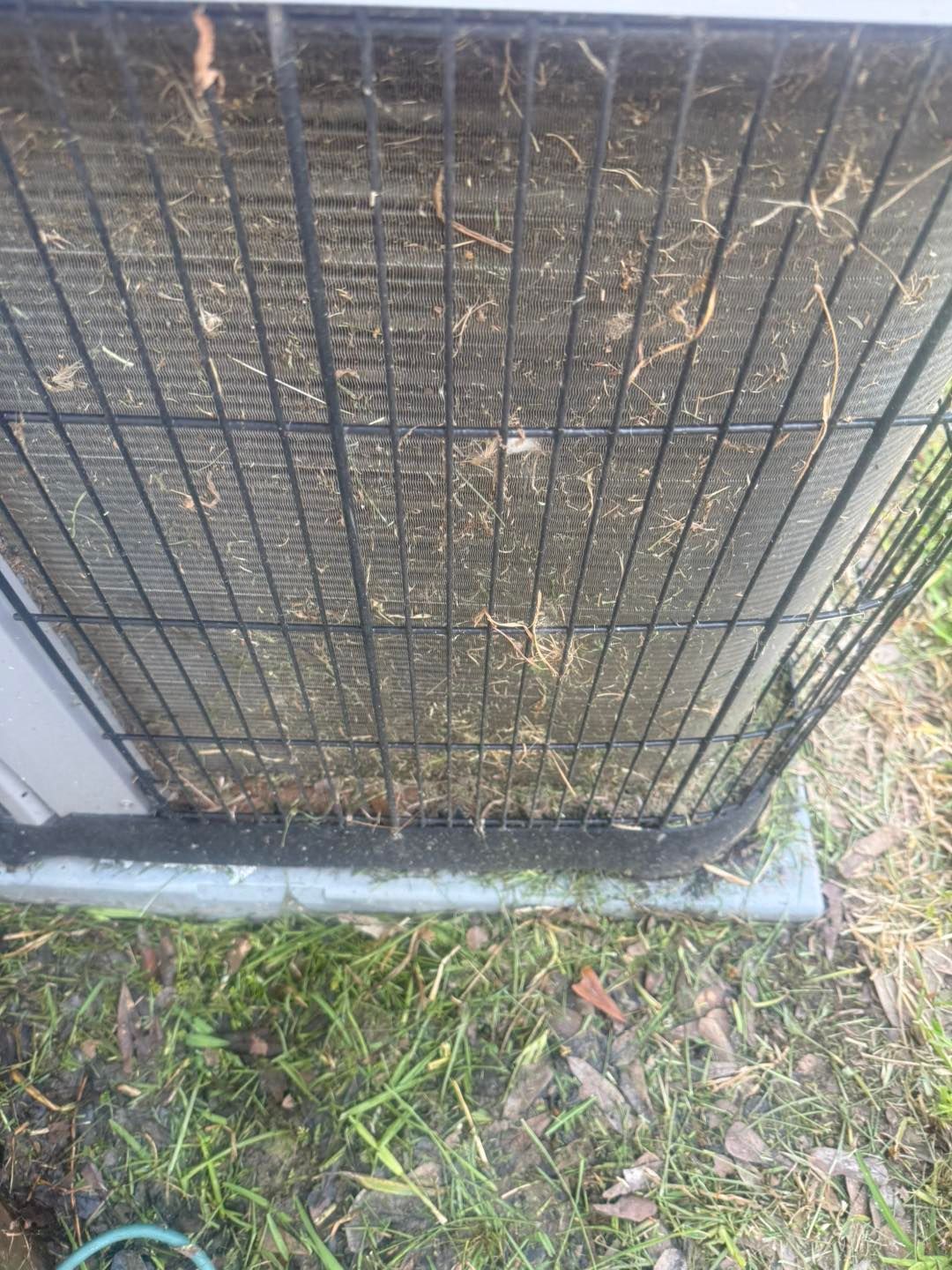 AC unit with a dirty, clogged condenser coil, surrounded by grass.