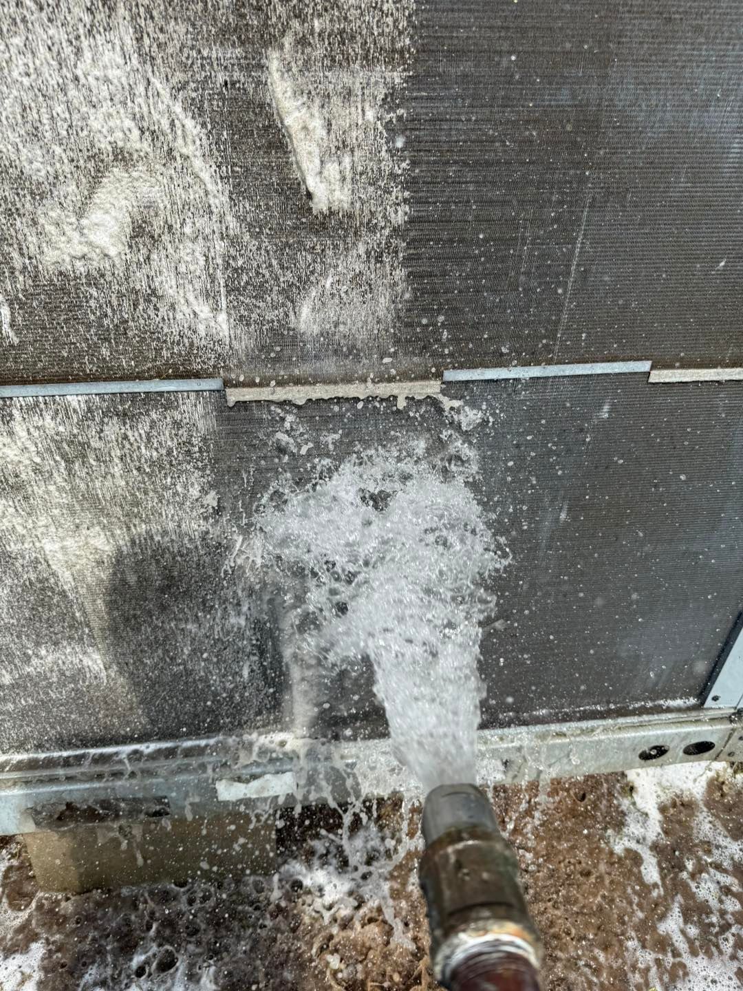 Cleaning an air conditioner coil with water, removing debris.