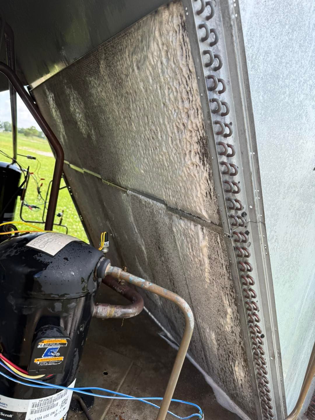 A dirty HVAC condenser coil with a compressor, in an outdoor setting.