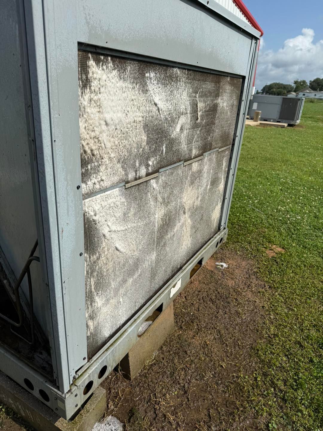 HVAC unit with dirty, white-coated filter on a grassy area under a blue sky.