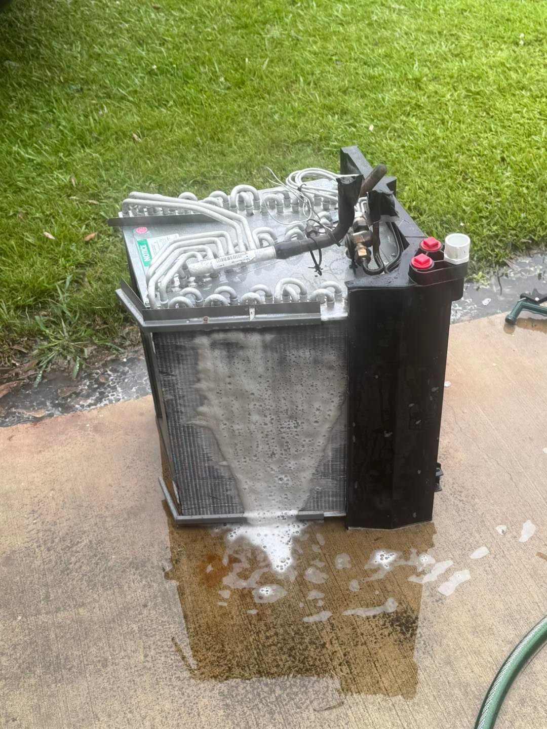 Air conditioning unit being cleaned outside with soapy water.