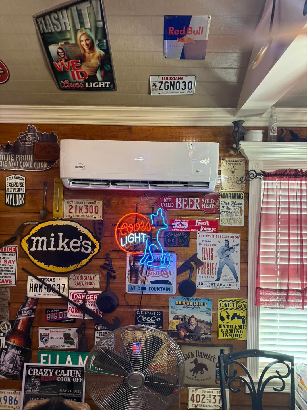 Wall decorated with signs and an air conditioner, a fan is in front of it.