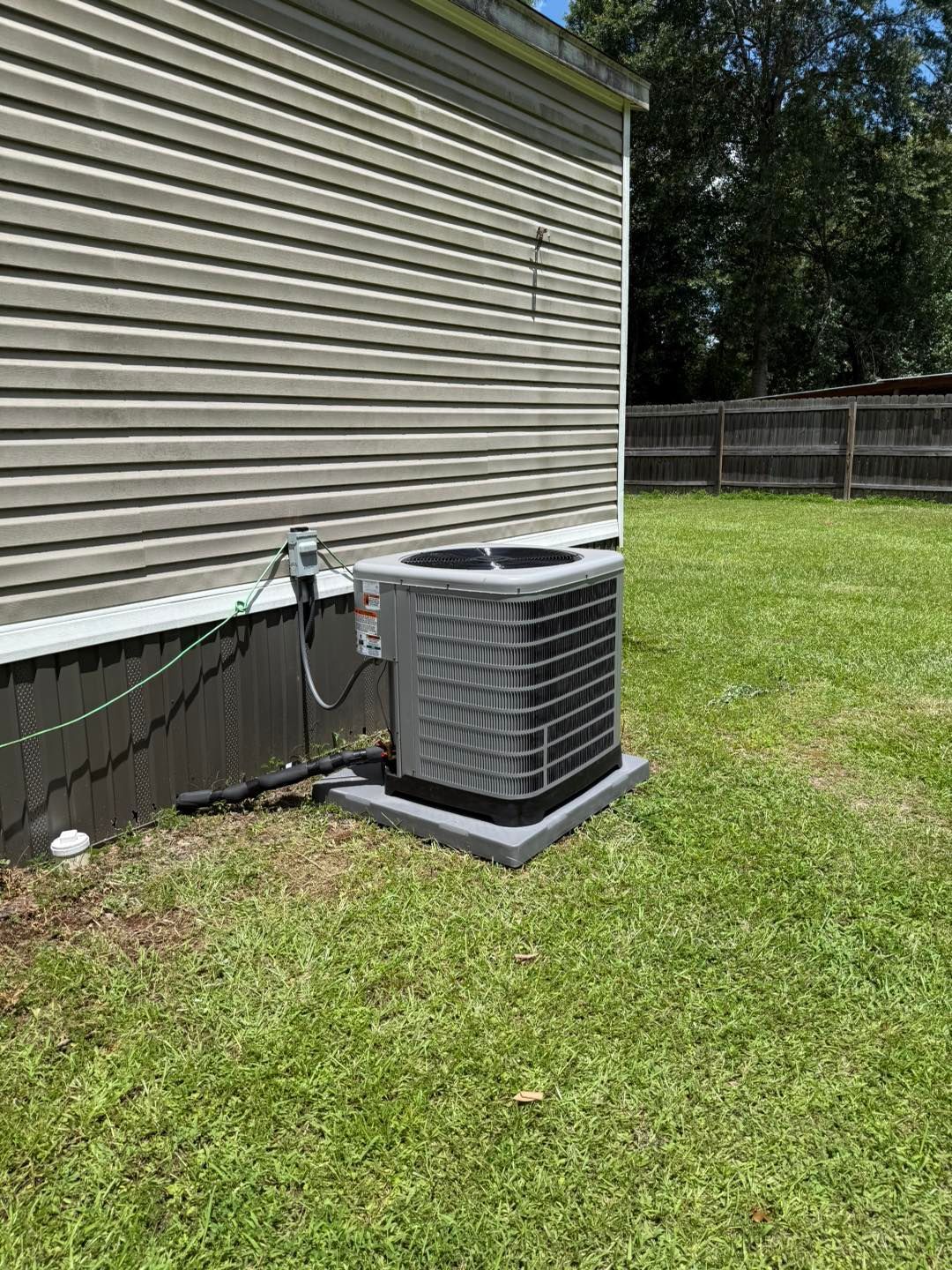 Exterior HVAC unit on a concrete pad next to a house with siding, in a grassy yard.