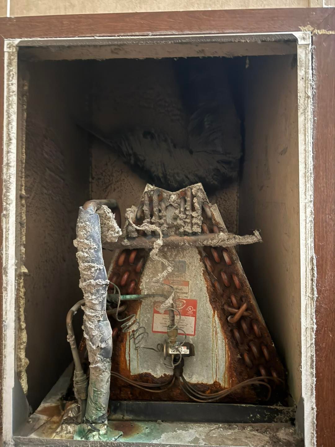 An old, corroded air conditioning unit in a wooden box. Rust and wear are visible on the unit's metal parts.