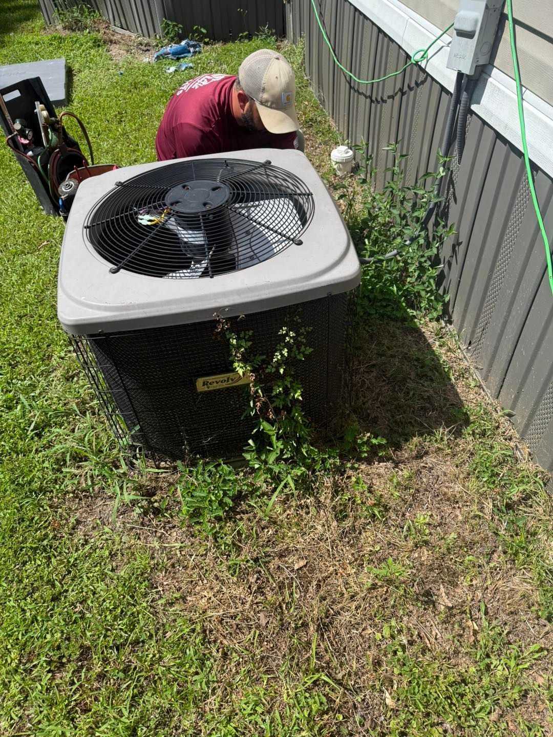 HVAC technician working on an air conditioning unit near a house.