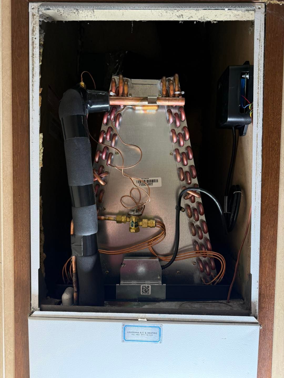 An air conditioning unit inside a wall, showing copper coils, black insulation, and wiring.