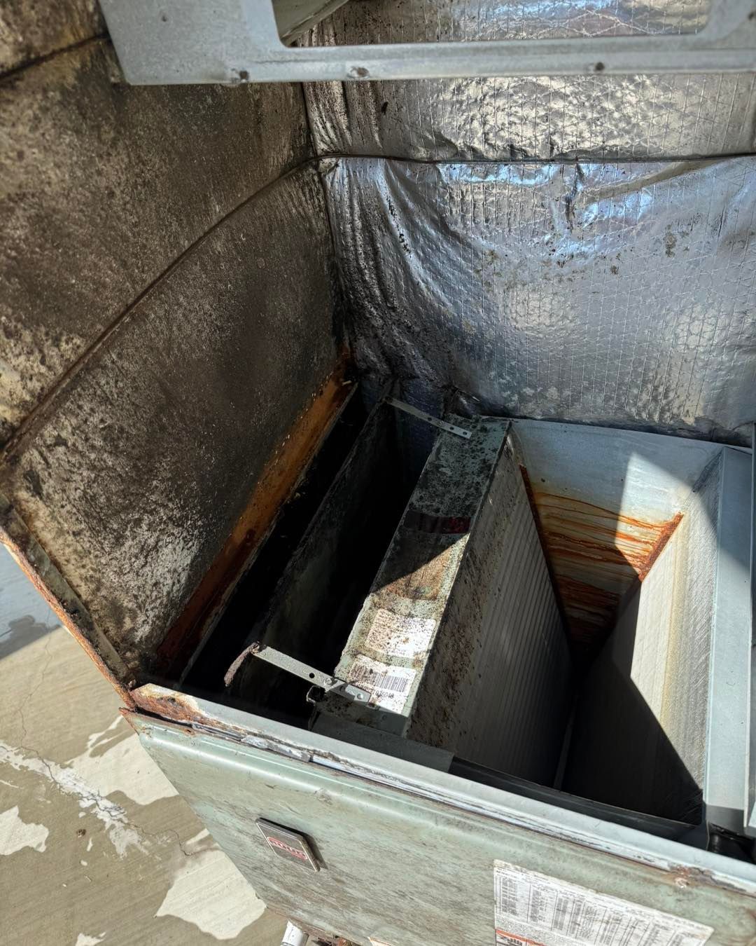 Interior view of a dirty, metal air handler with visible rust and debris.