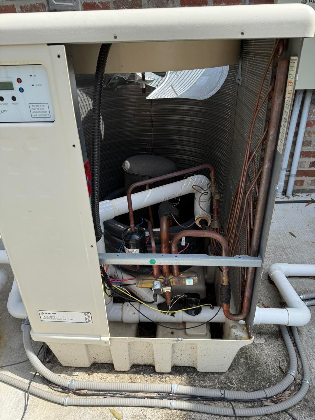 Swimming pool heat pump with open access panel, revealing copper pipes, electrical components, and compressor.