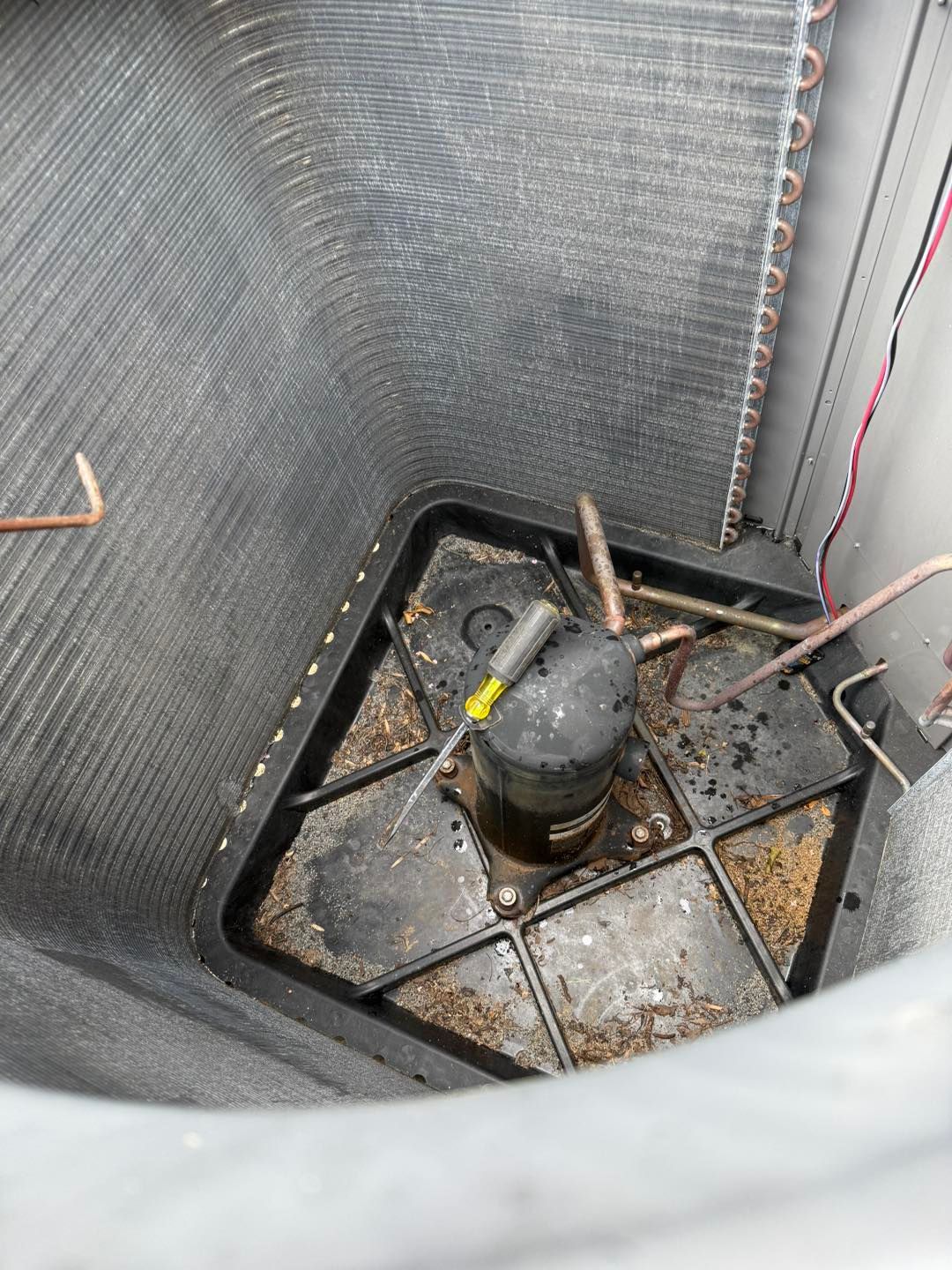 A dirty air conditioning compressor in an outdoor unit, surrounded by metal fins and tubes.