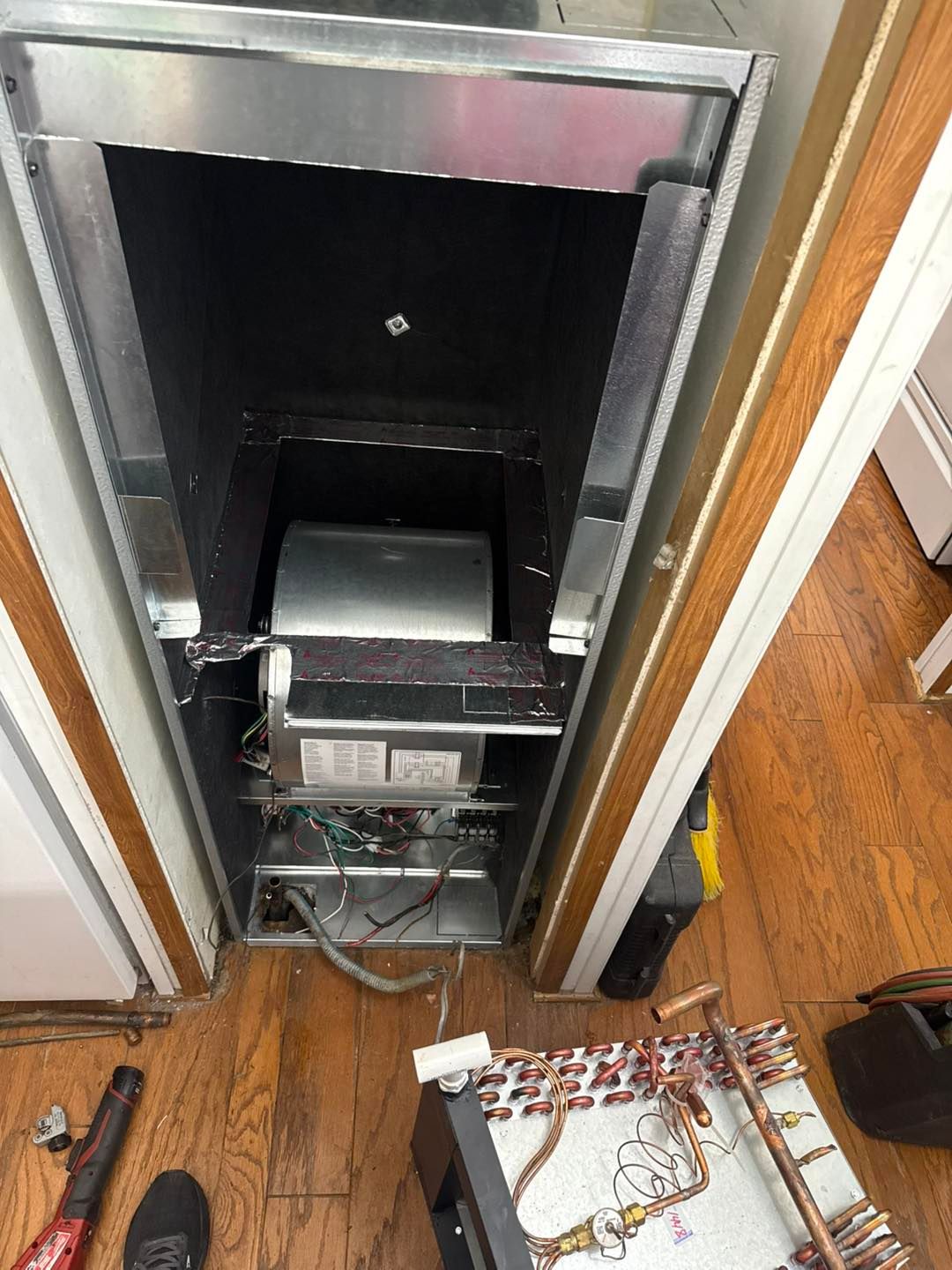 Open air conditioning unit in a doorway showing fan, ductwork, and electrical components.