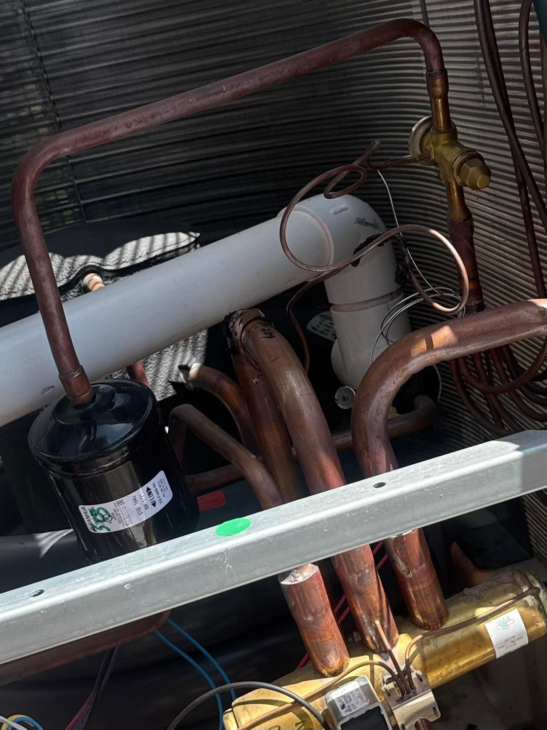 Copper tubing and white cylinder within an air conditioning unit.