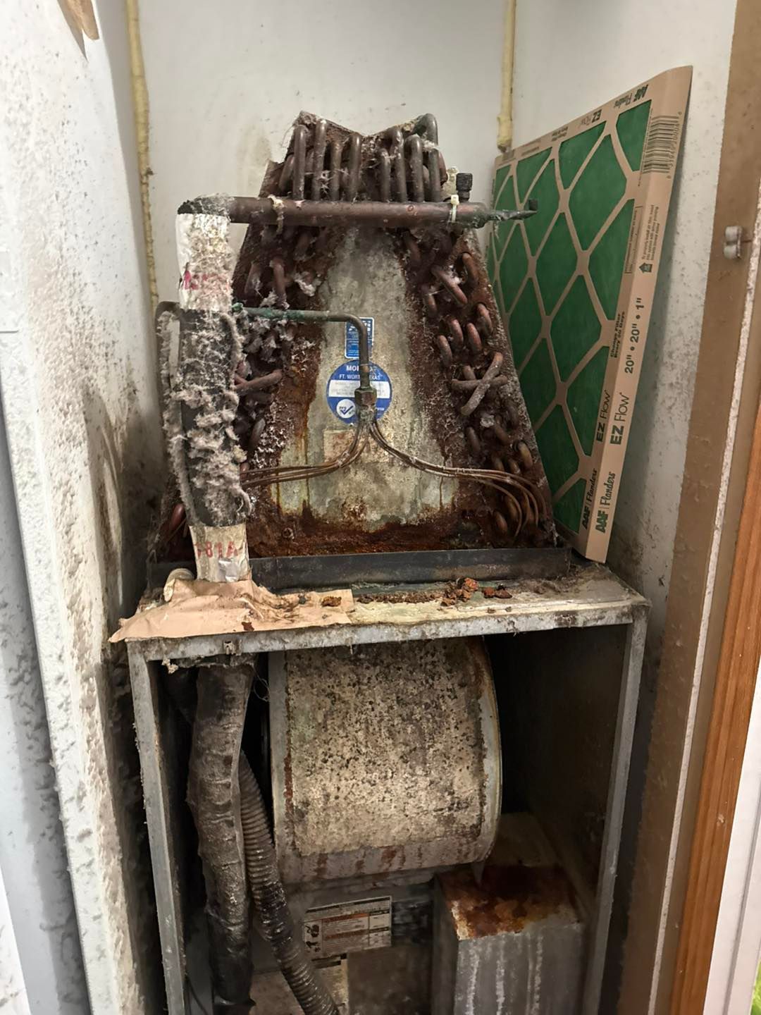 Corroded HVAC unit in a utility closet with a dirty air filter and metal frame.