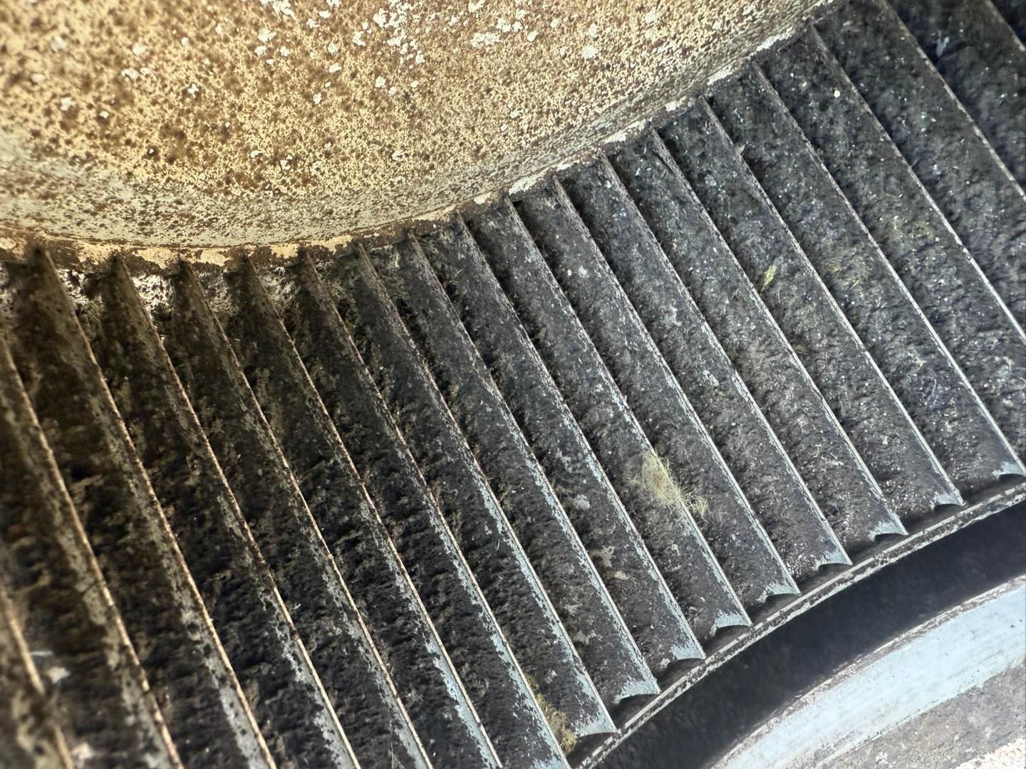 Close-up of a dark, grooved belt, possibly a fan or engine belt, with a dusty, textured metal surface.