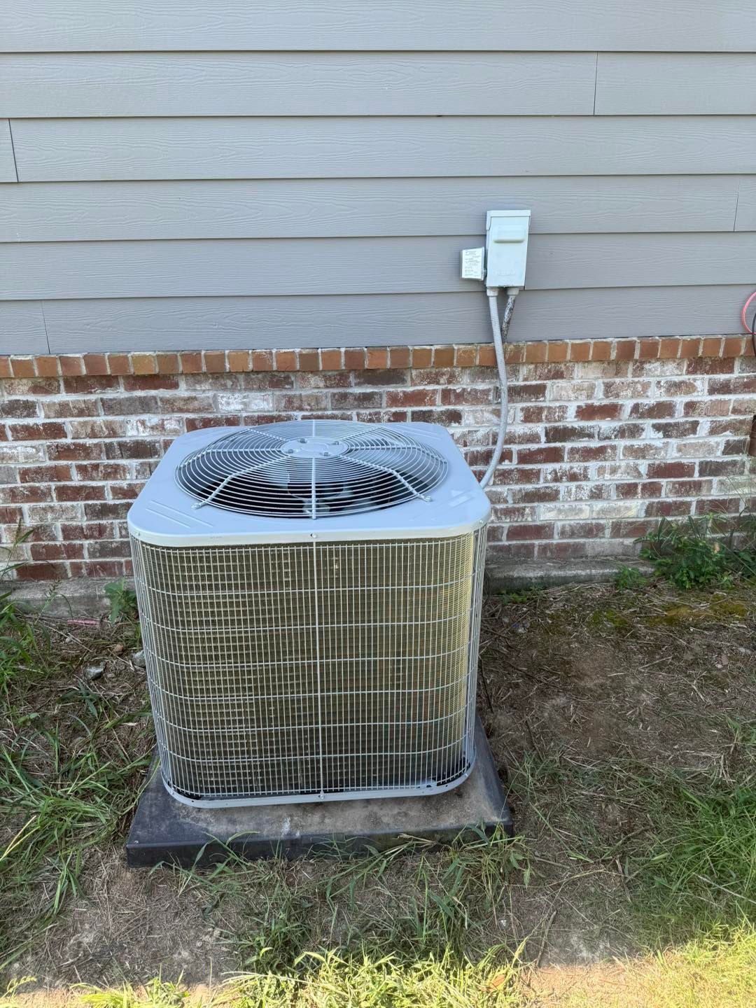 Outdoor air conditioning unit against a brick and siding wall.