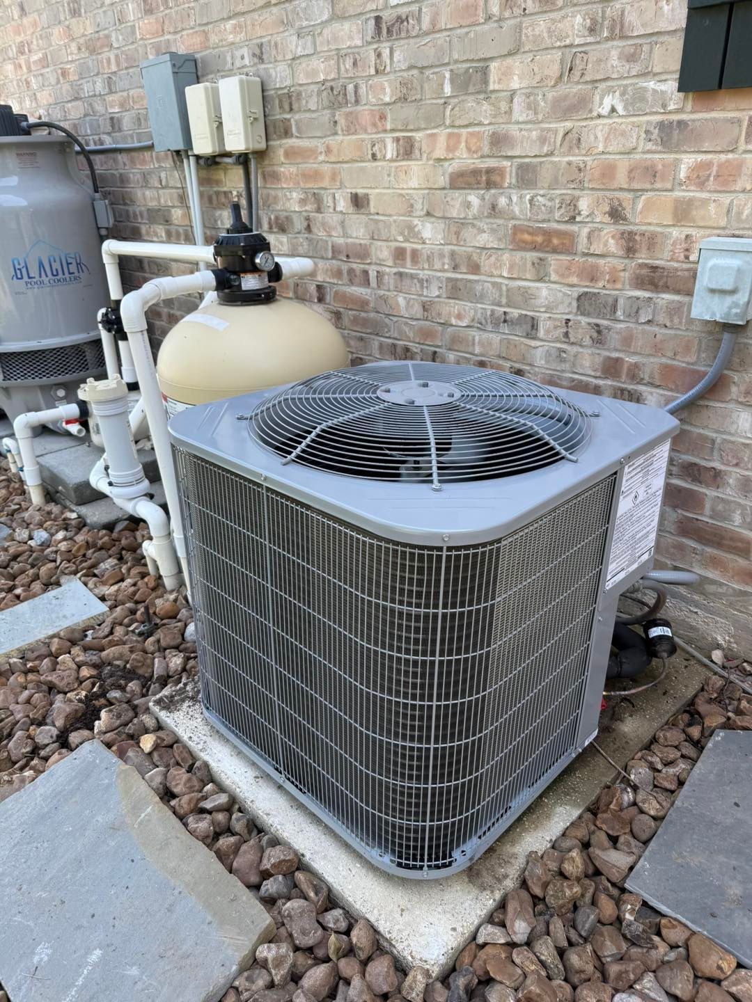 Air conditioning unit against a brick wall, next to pool equipment.