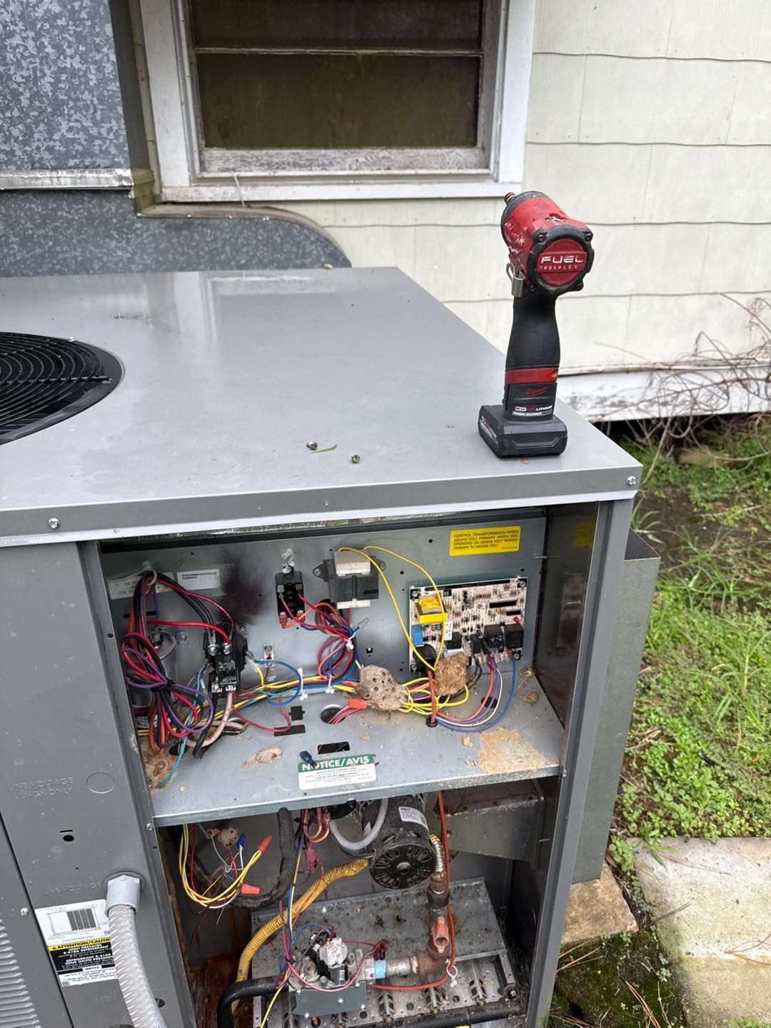 Open air conditioner unit with exposed wiring, and a red drill on top.