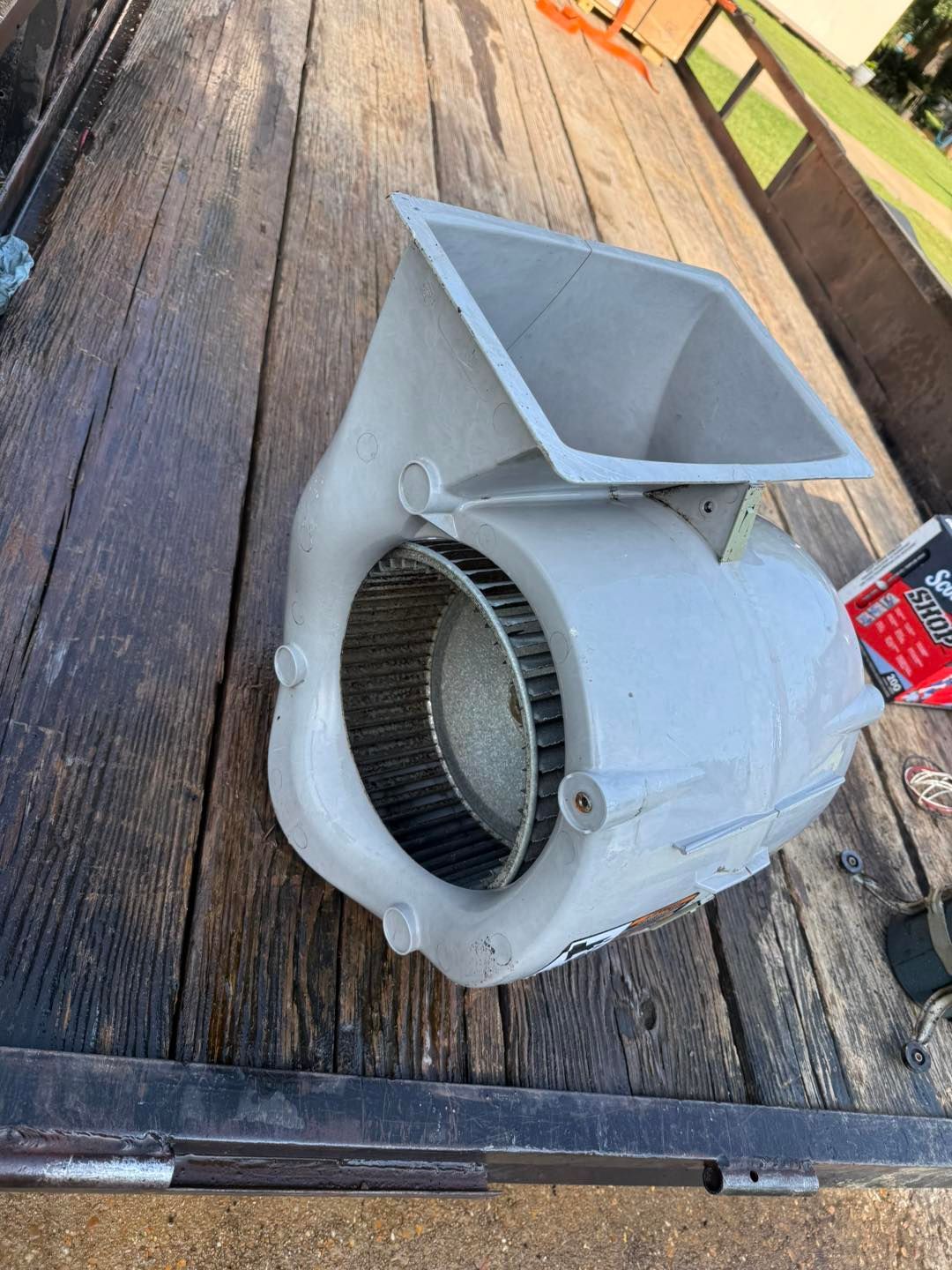 A gray centrifugal blower sits on a weathered wooden surface.